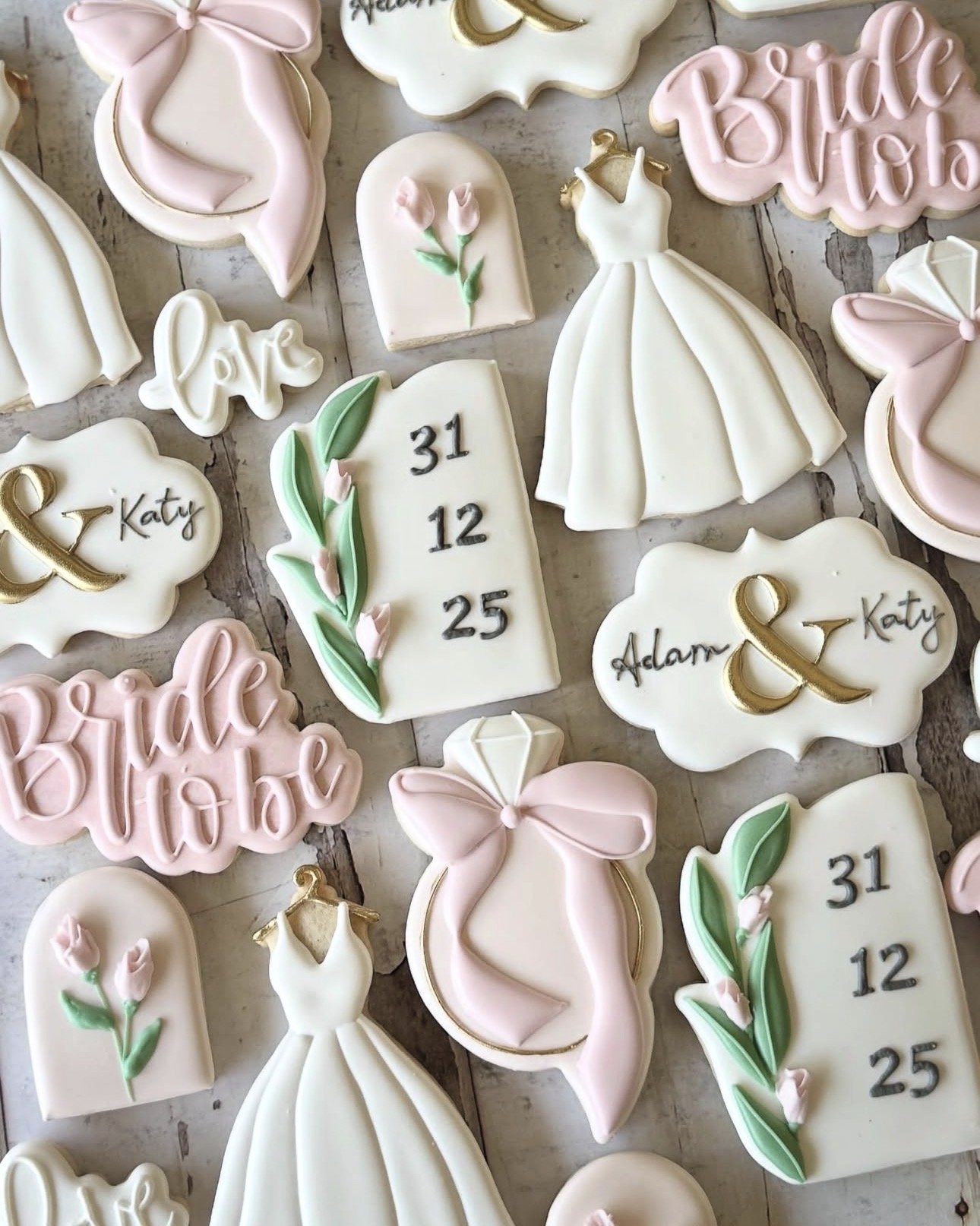 Assortment of pastel pink and white decorated cookies featuring bridal gowns, bows, flowers, wedding dates, and names Adam and Katy