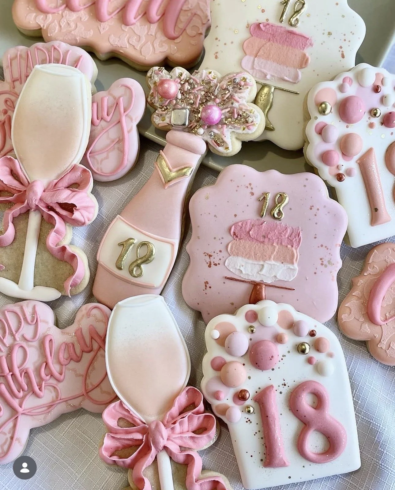 Assorted pink and white pink-themed decorated cookies with bows, popsicles, sprinkles, and gold number 18 accents