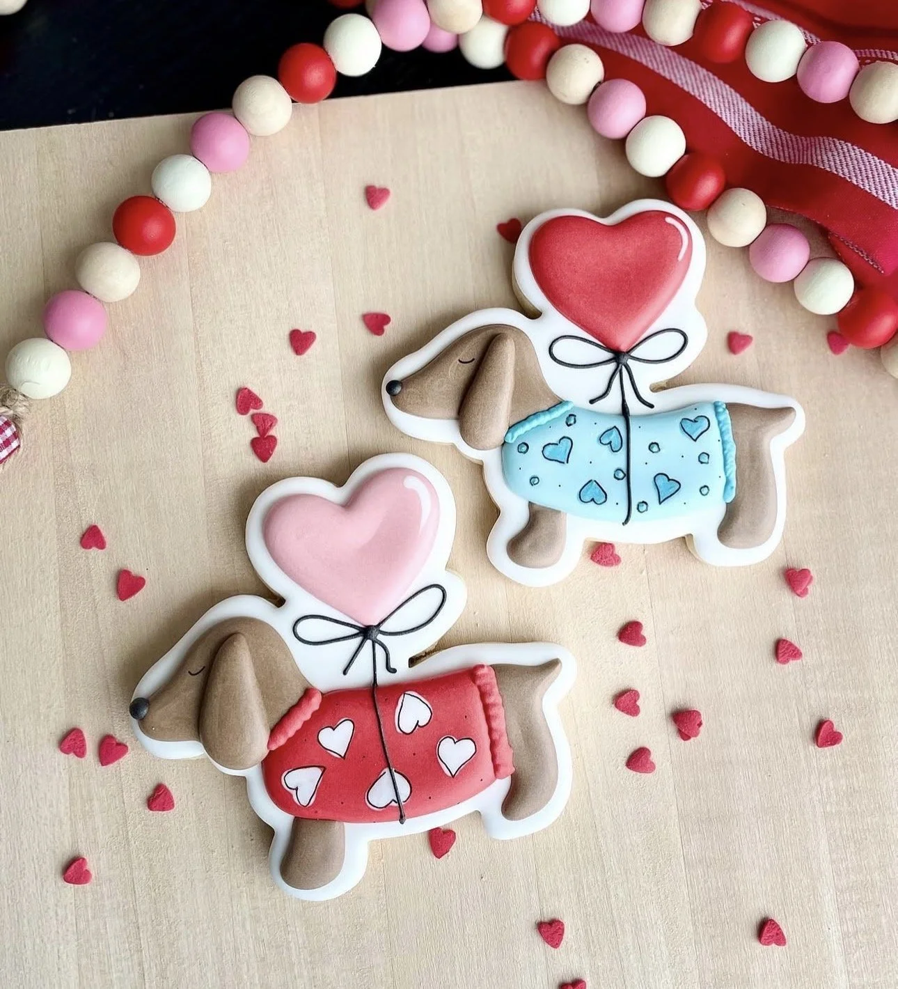 Decorated dog-shaped Valentine’s Day cookies with heart balloons, surrounded by red heart sprinkles and pastel candies.