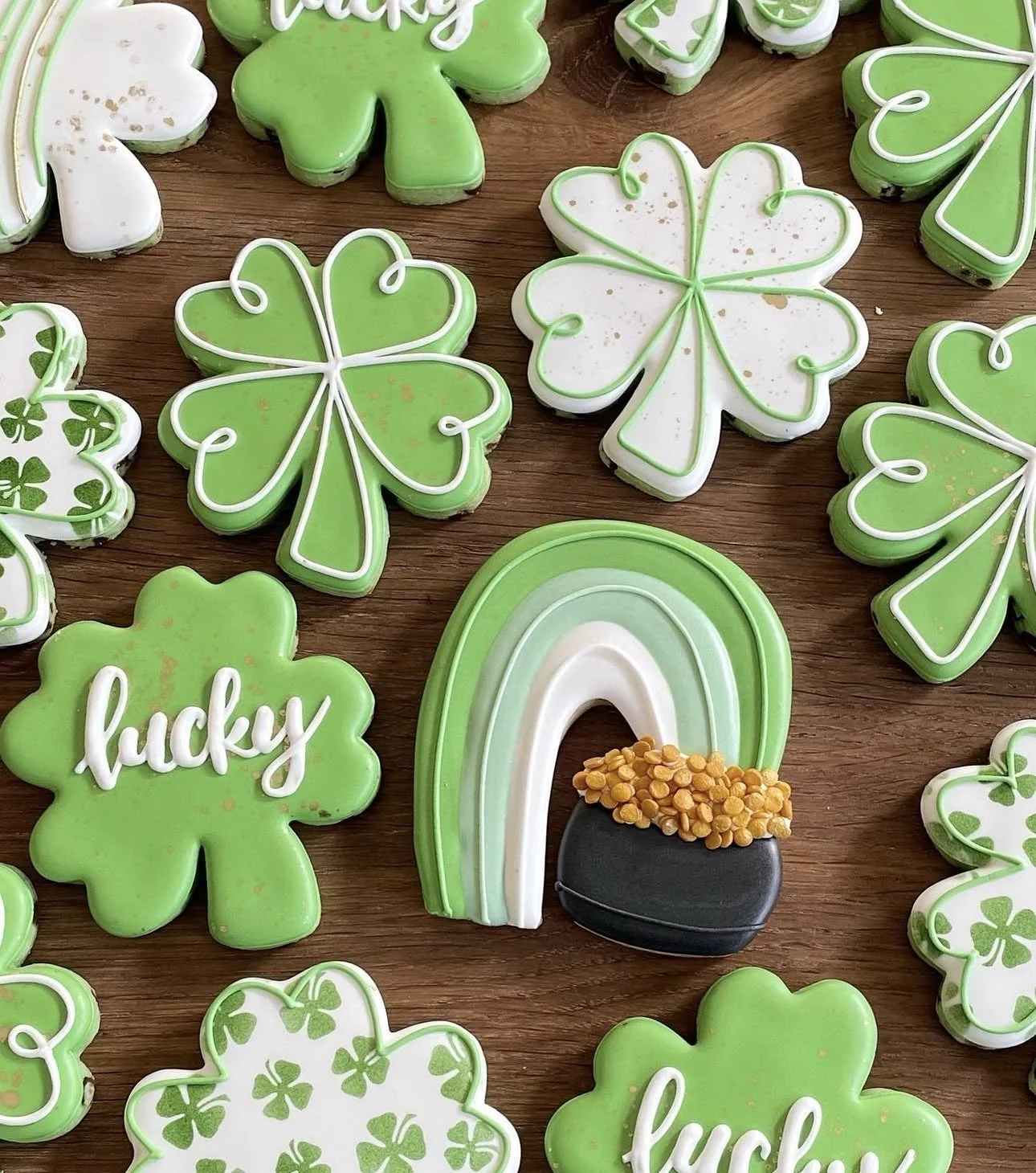 St. Patrick’s Day-themed decorated sugar cookies, including green shamrocks, hearts, a rainbow, and a pot of gold on a wooden table