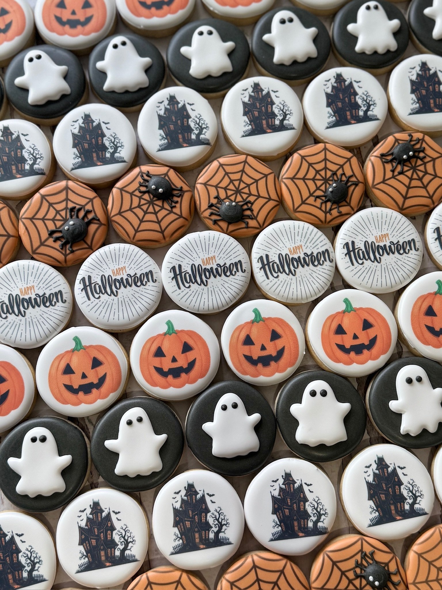 Assorted Halloween sugar cookies decorated with pumpkins, ghosts, haunted houses, spiderwebs, spiders, and “Happy Halloween” lettering.