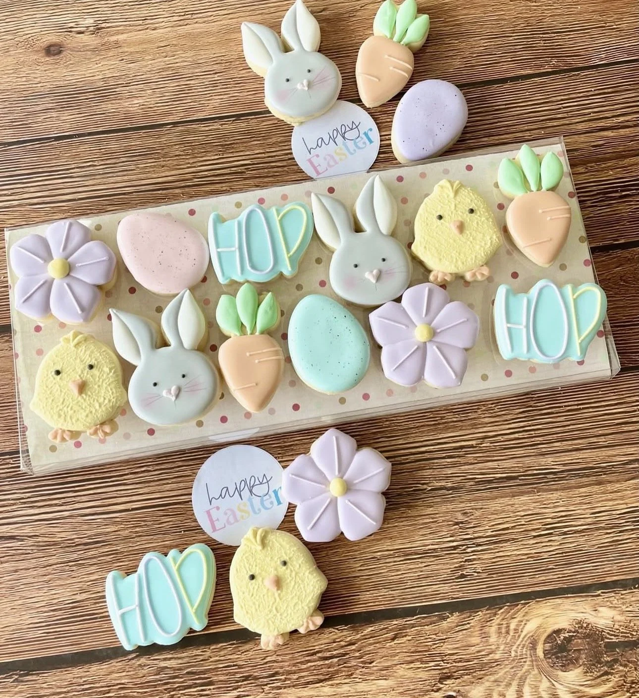 Decorated Easter cookies shaped like bunnies, chicks, carrots, flowers, eggs, and the word “Easter” on a wooden table.