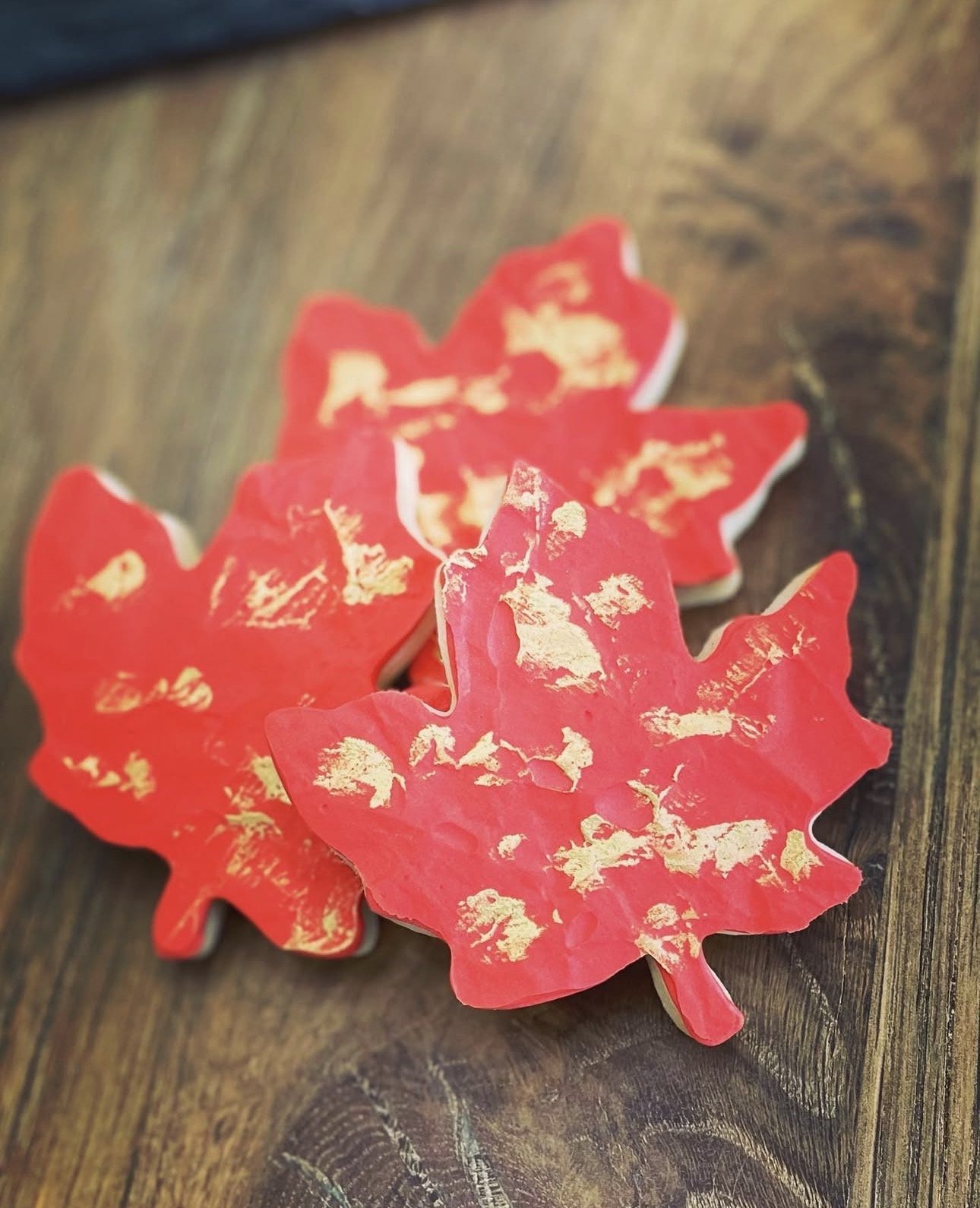 Three red maple leaf-shaped decorations with gold accents on a dark wooden table