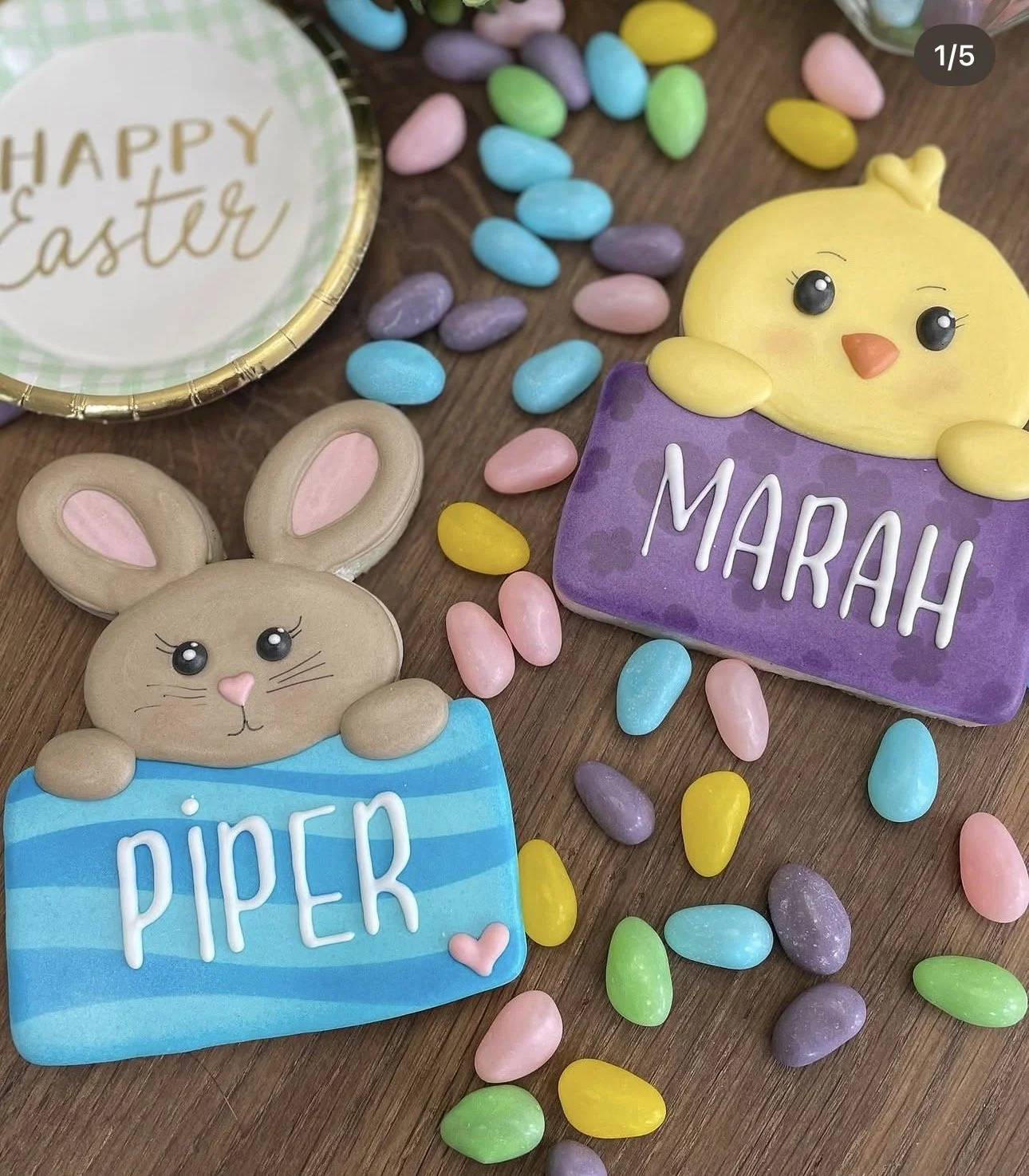 Easter-themed cookies featuring a chick labeled Mariah and a bunny labeled Piper, surrounded by colorful candy eggs and a Happy Easter plate.
