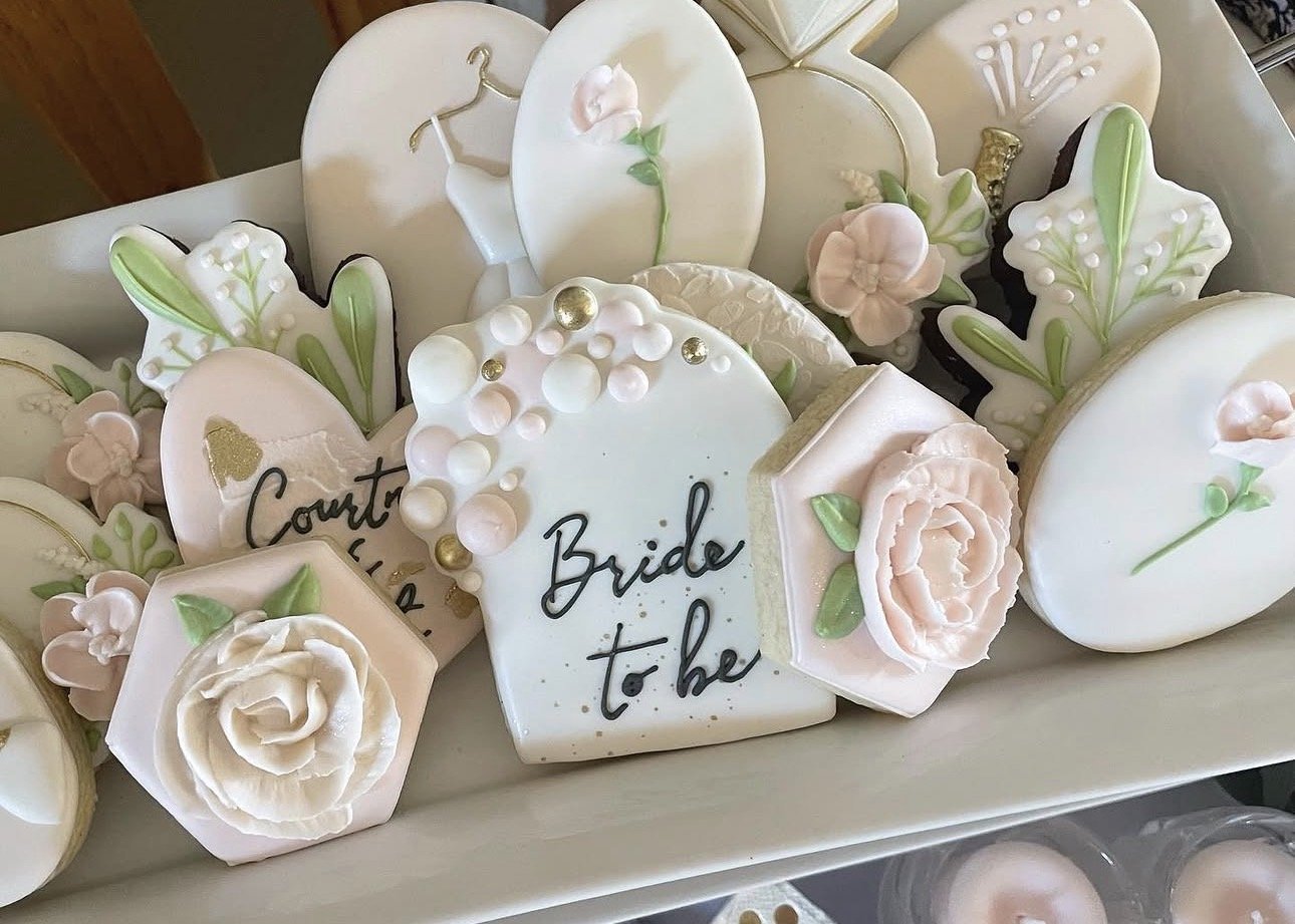 Decorated bridal shower sugar cookies with flowers, wedding rings, and a cookie reading “Bride to be.”