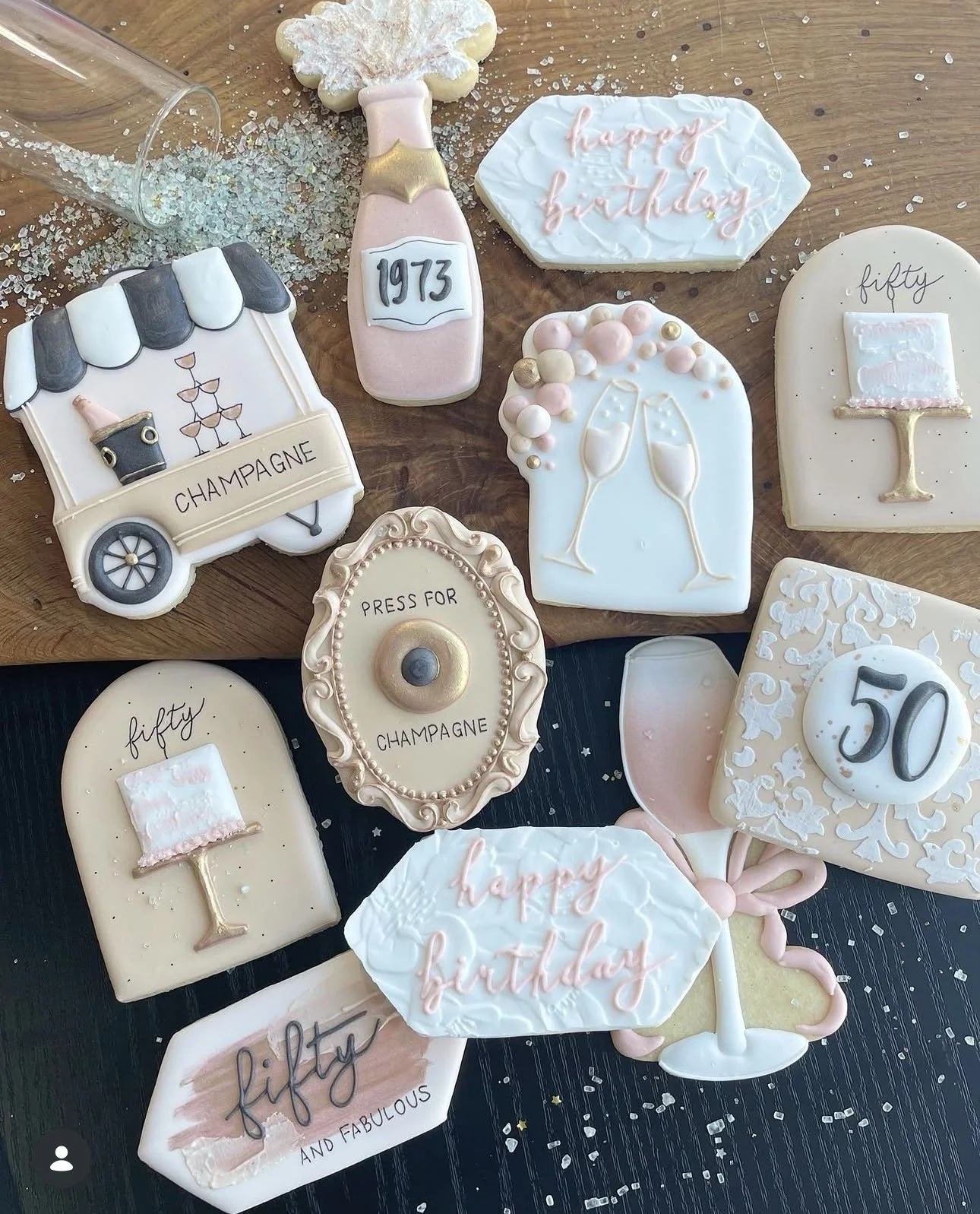 Decorated birthday cookies for a 50th birthday celebration, featuring champagne bottles, glasses, a champagne cart, birthday messages, and the year 1973.