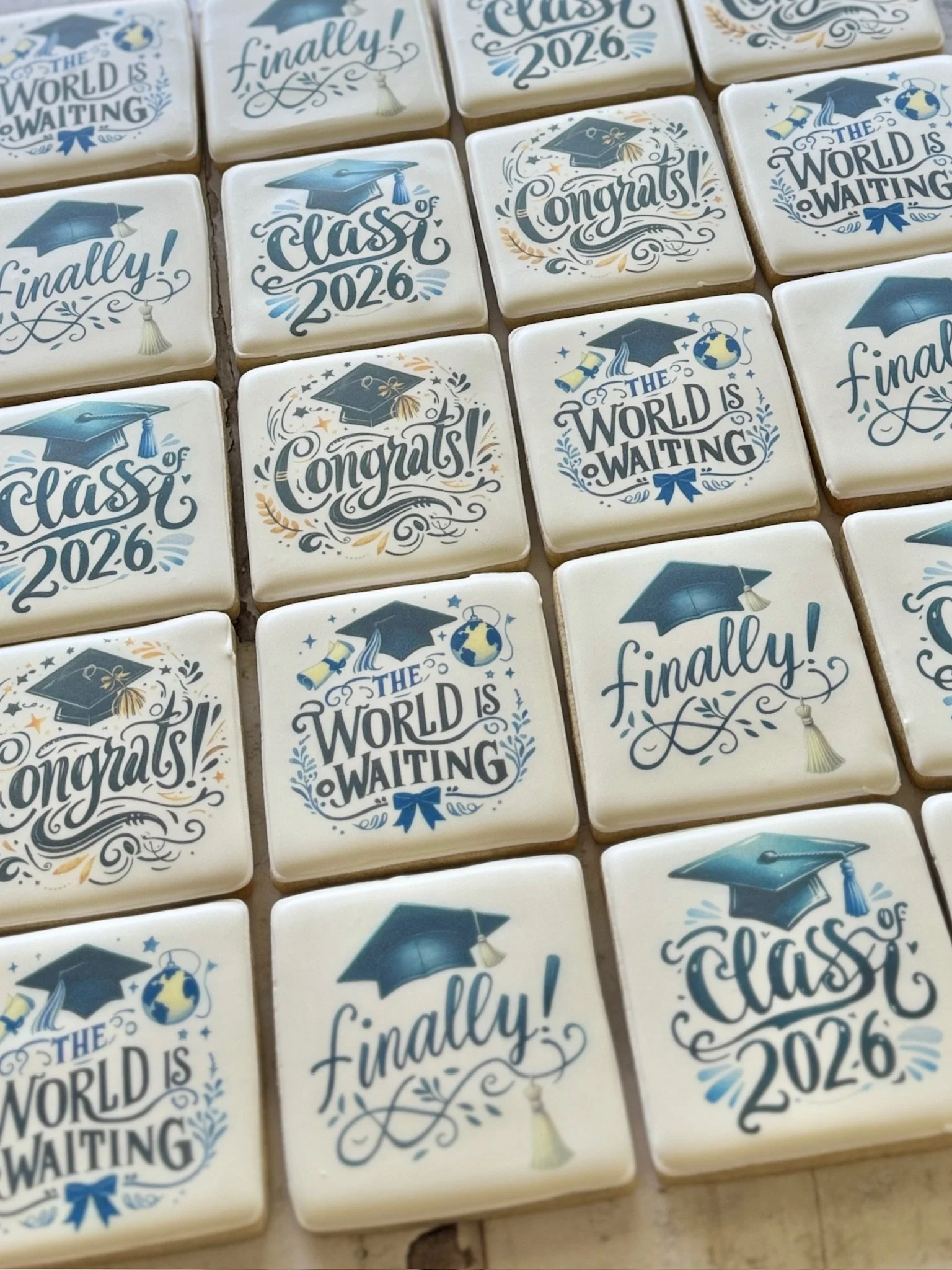 Decorated graduation cookies featuring caps, diplomas, and messages including “Class of 2026,” “Congrats!” and “The world is waiting.”