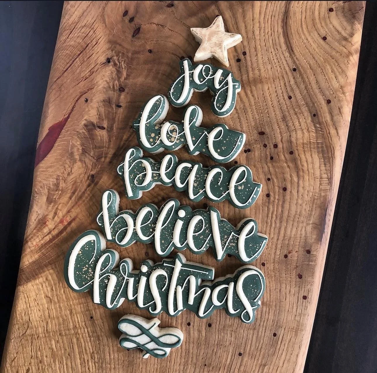Handcrafted Christmas decoration reading “Joy, love, peace, believe, Christmas” on a rustic wooden board, with a star and bow.