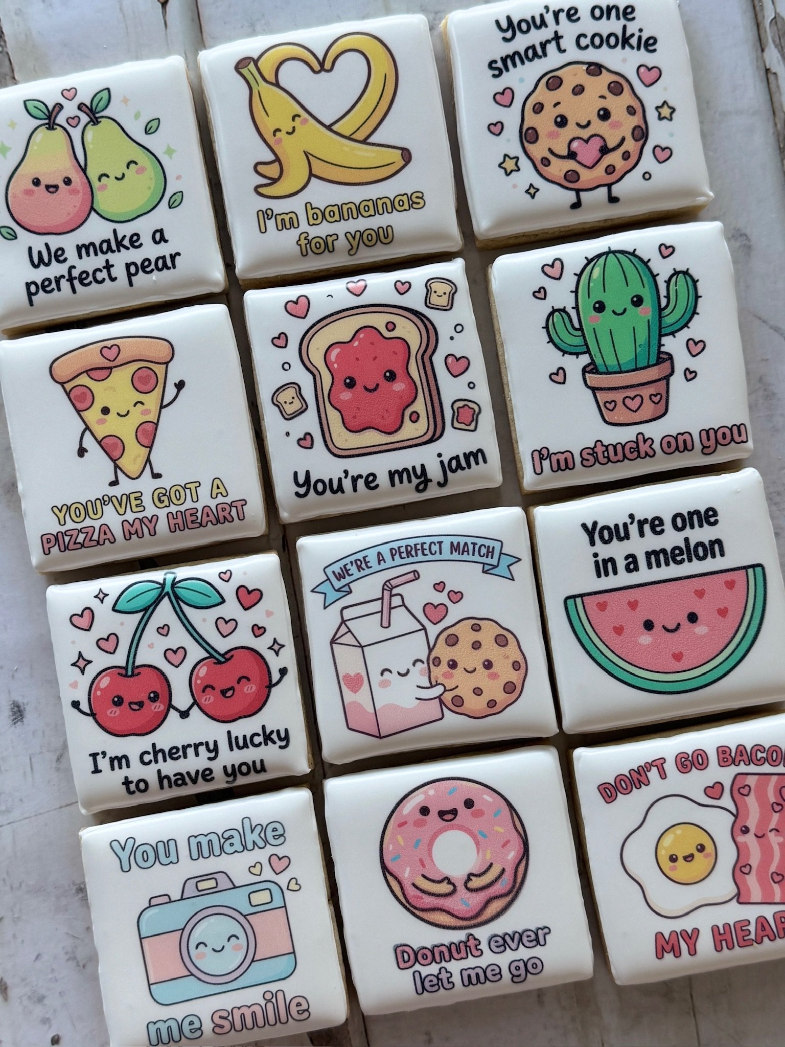 Assortment of decorated rectangular cookies with cute fruit and food illustrations, including pears, bananas, cookies, pizza, toast, cactus, cherries, watermelon, donuts, and playful pun messages.