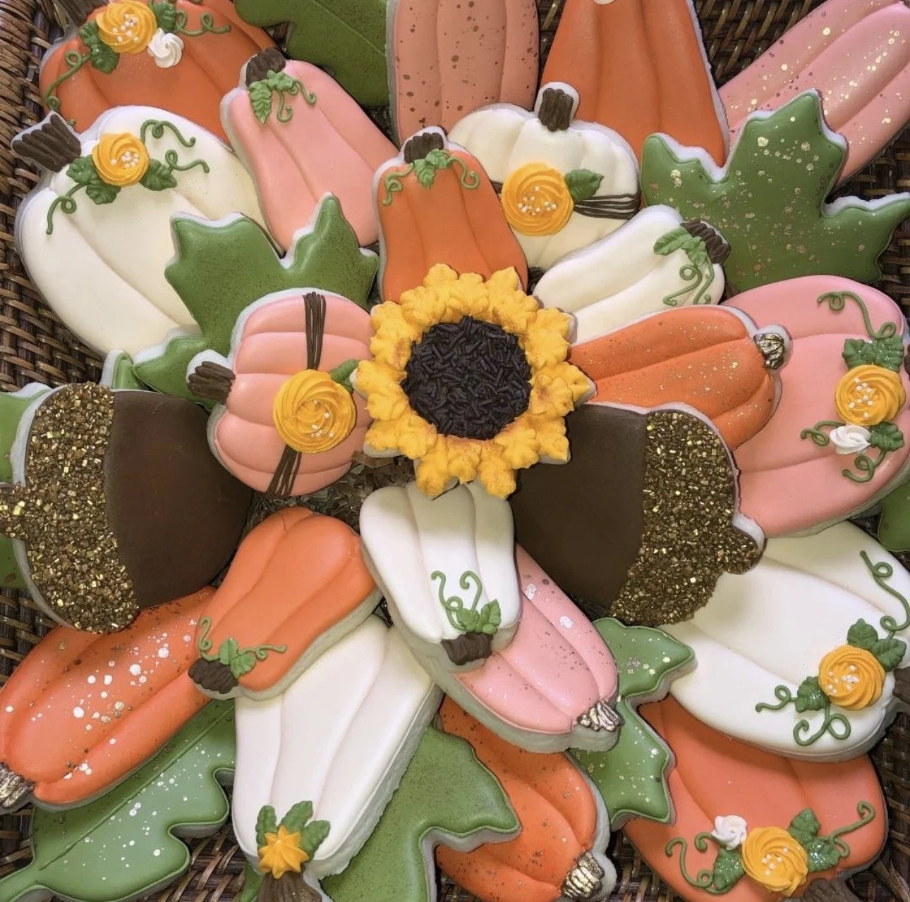 Assortment of colorful pumpkin-shaped decorated sugar cookies surrounding a sunflower cookie in a basket