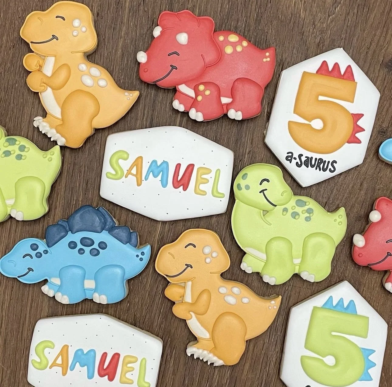 Colorful dinosaur-shaped cookies and name plaques reading “SAMUEL” on a wooden surface.