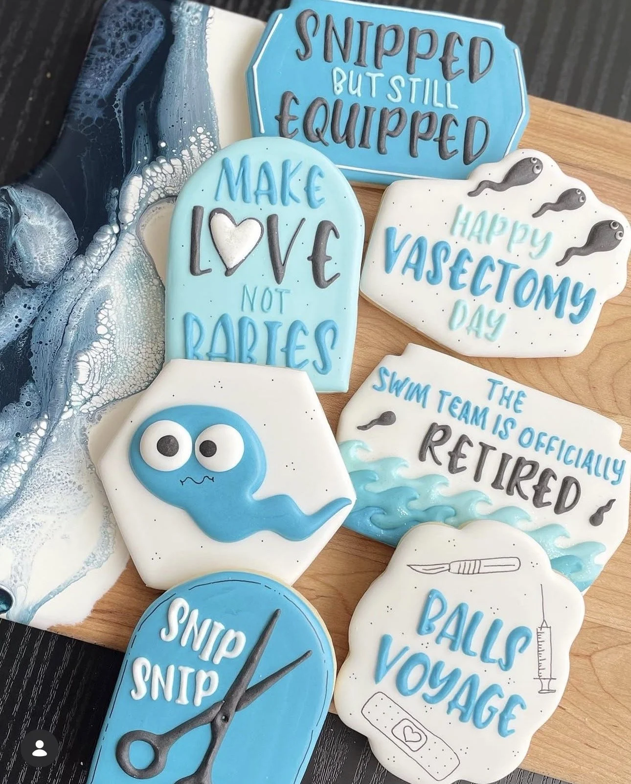 Decorated blue and white nursing graduation cookies with medical-themed designs and messages, including “Snipped but still equipped,” “Make love not babies,” and “Happy Vasectomy Day.”