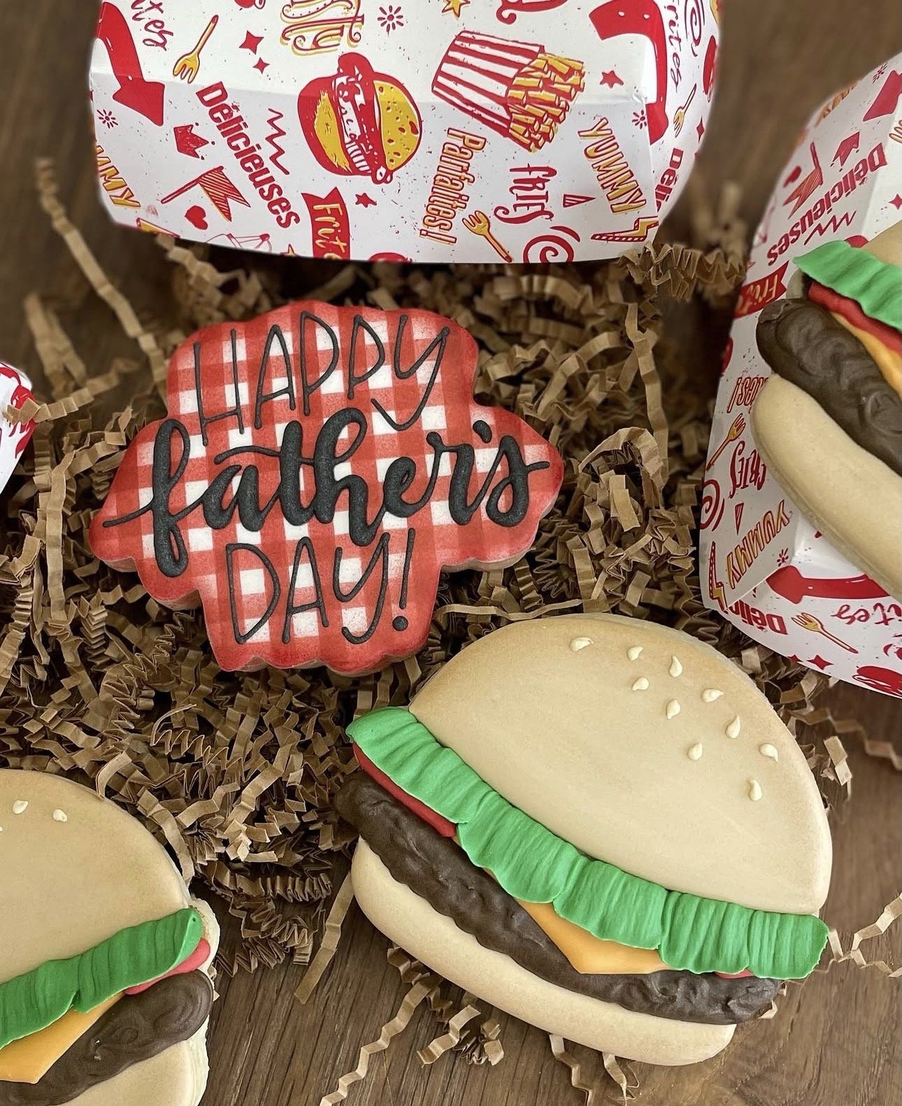 Decorated burger-themed gift box filled with shredded paper, hamburger-shaped cookies, and a red-and-white “Happy Father’s Day” cookie.