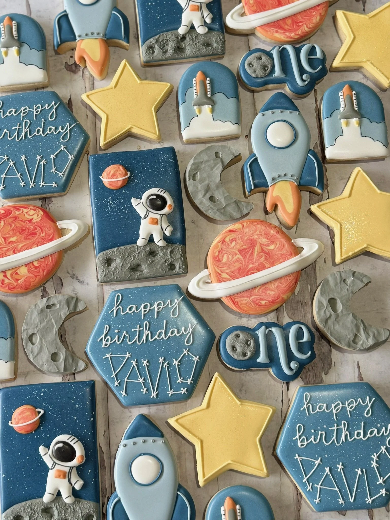 Space-themed decorated sugar cookies featuring rockets, astronauts, Saturn-like planets, stars, moons, and “happy birthday” galaxy designs.