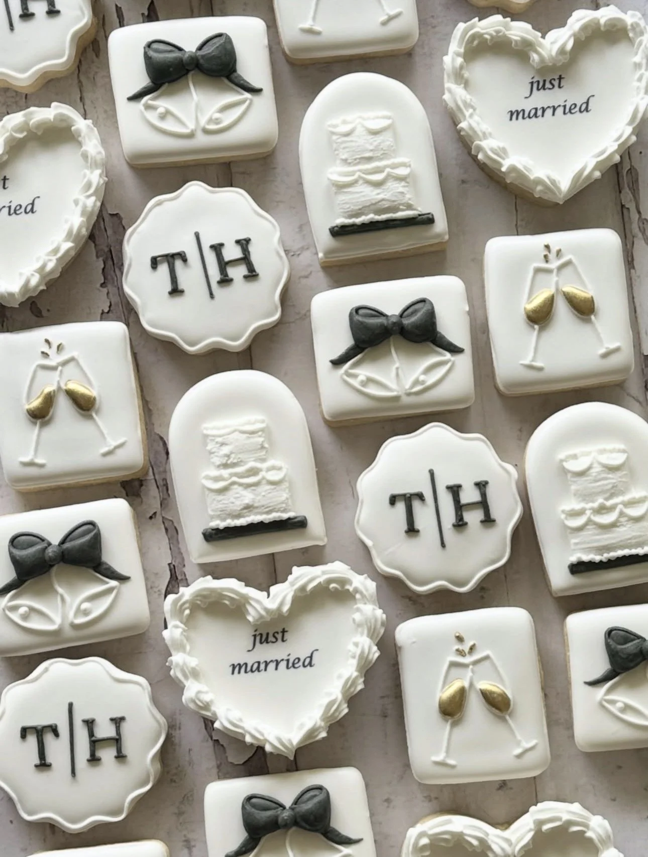 Wedding-themed decorated sugar cookies featuring wedding cakes, champagne glasses, black bow ties, and “just married” and “TH” designs