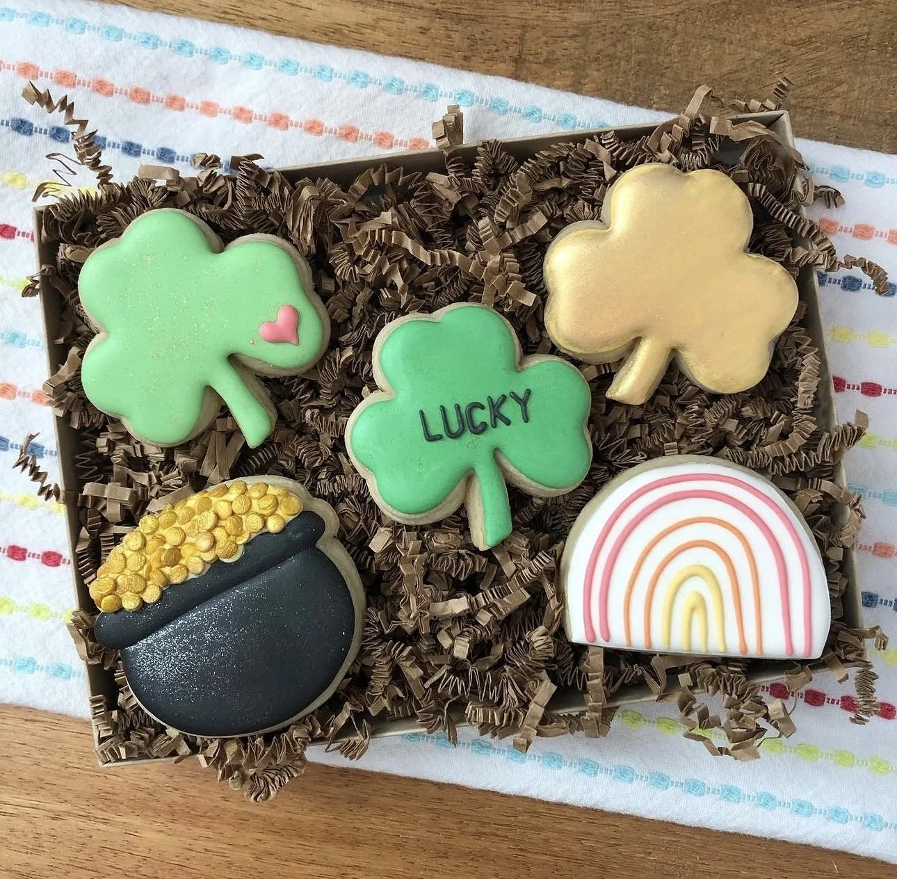 St. Patrick’s Day-themed decorated sugar cookies in a box, featuring shamrocks, a pot of gold, a rainbow, and a cookie labeled “LUCKY.”