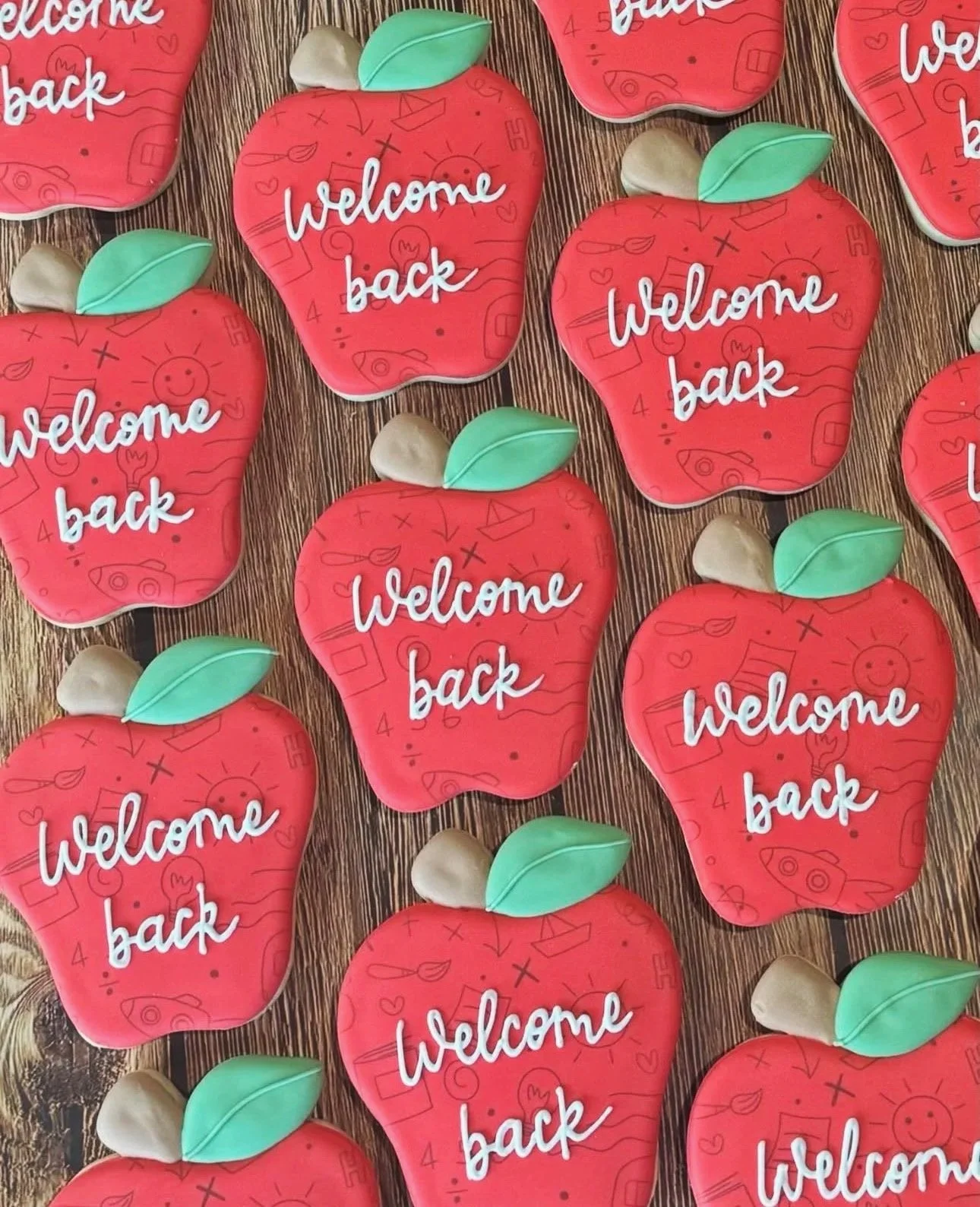 Red apple-shaped back-to-school cookies with green leaves and white “Welcome back” lettering on a wood-grain surface