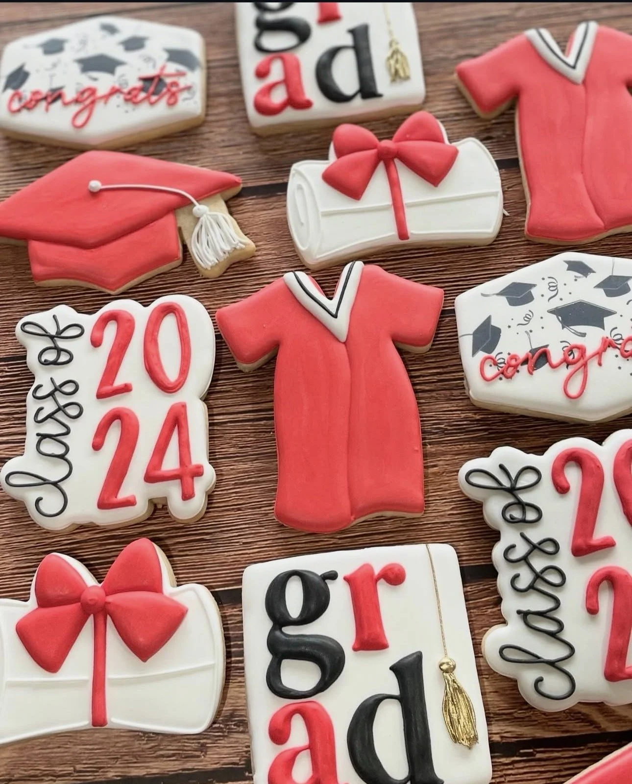 Graduation-themed decorated cookies featuring red caps and gowns, diplomas with bows, class years, and congratulatory messages on a wooden table