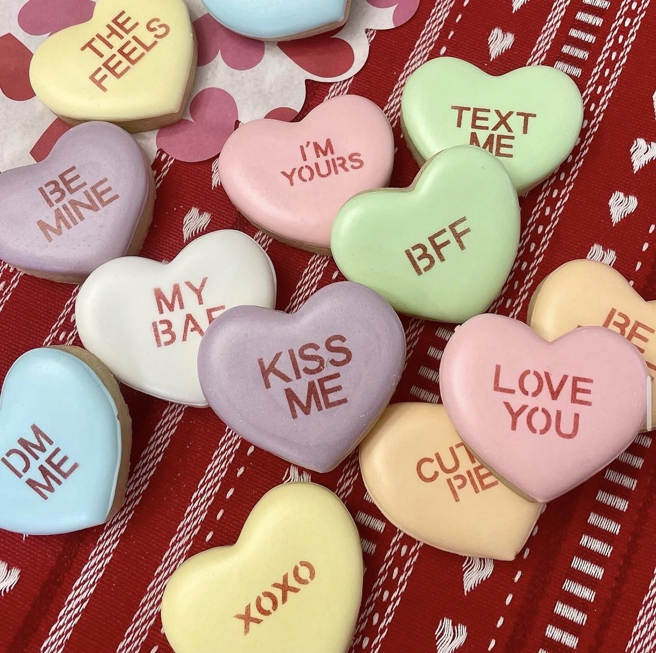 Colorful heart-shaped conversation candies with romantic messages on a red patterned fabric background