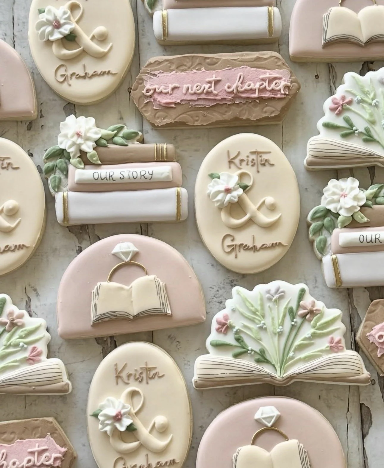Decorated wedding-themed sugar cookies featuring books, flowers, wedding rings, and messages including “our next chapter” and “Our Story.”