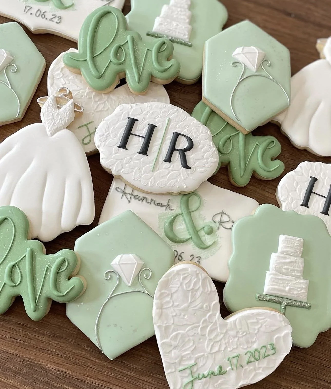 Assorted mint green and white wedding-themed decorated sugar cookies, including wedding dresses, rings, hearts, and monogrammed initials.