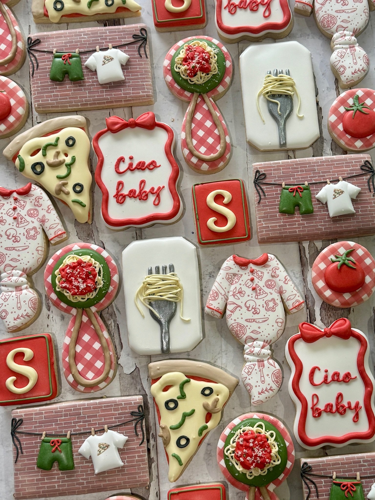 Assortment of colorful baby shower cookies, including “Ciao baby” plaques, tomato pasta plates, baby clothes, onesies, and pizza slices.