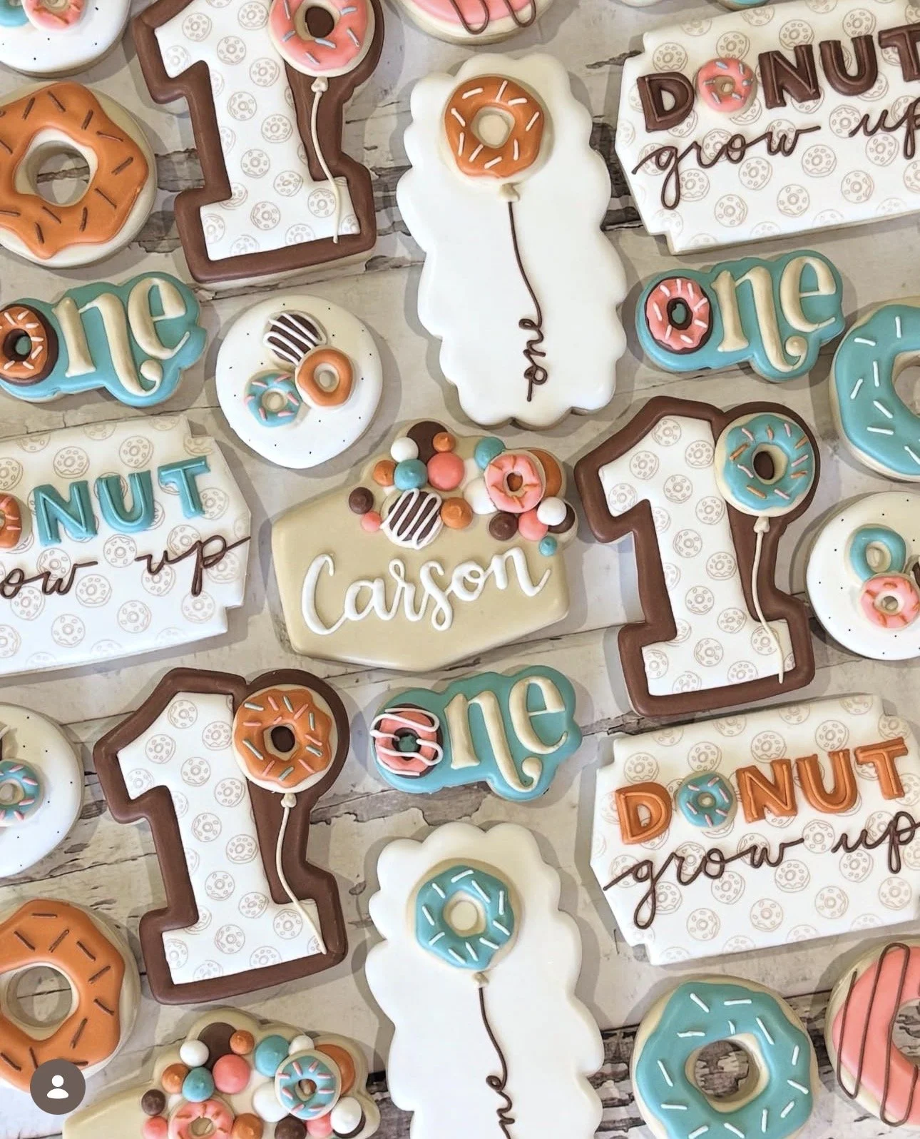 Colorful donut-themed cookies and treats arranged on a rustic wooden surface, including personalized “Carson” cookie and “Donut grow up” message cookies.