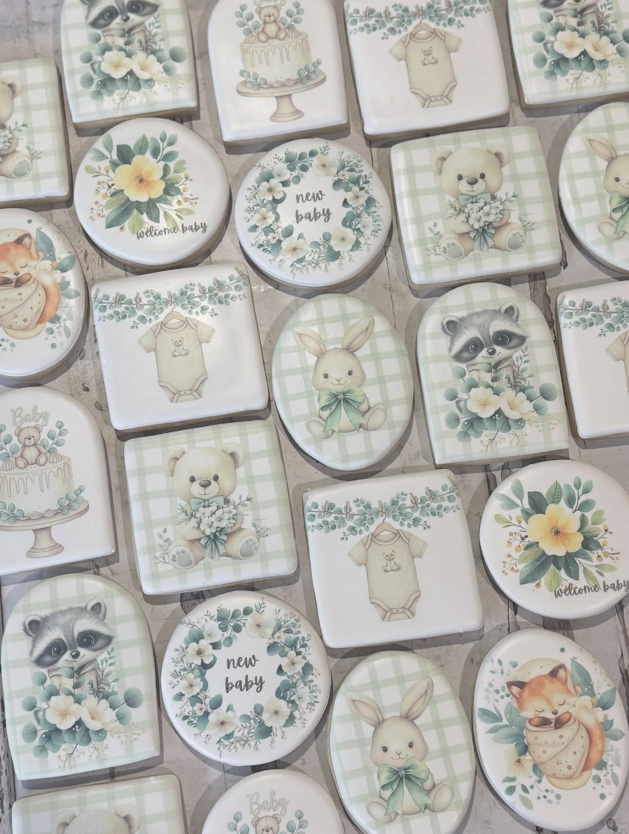 Hand-painted baby shower cookies featuring teddy bears, bunnies, raccoons, foxes, floral designs, cakes, onesies, and “new baby” messages.