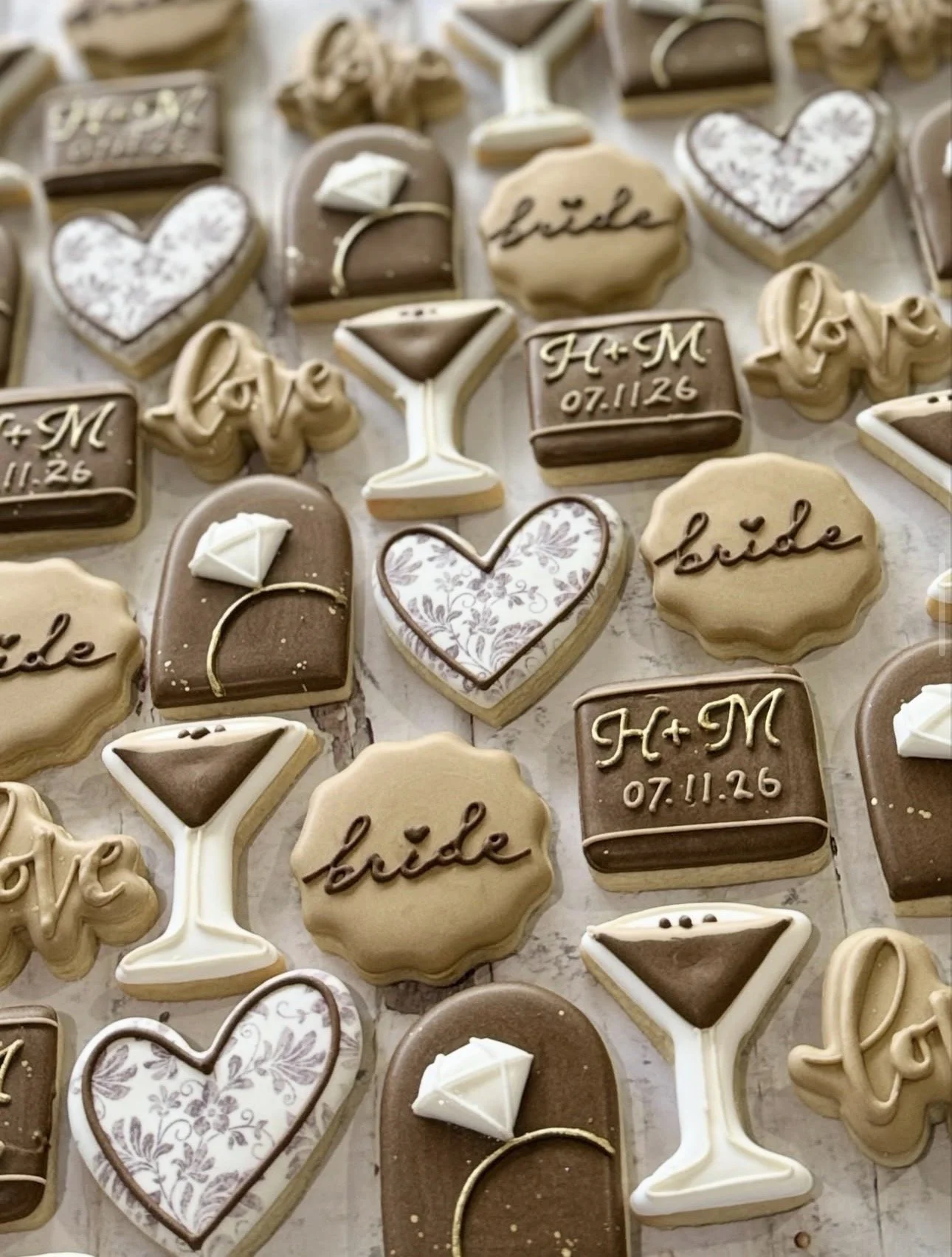 Assorted wedding-themed decorated sugar cookies featuring hearts, champagne glasses, rings, love lettering, and personalized initials with a date