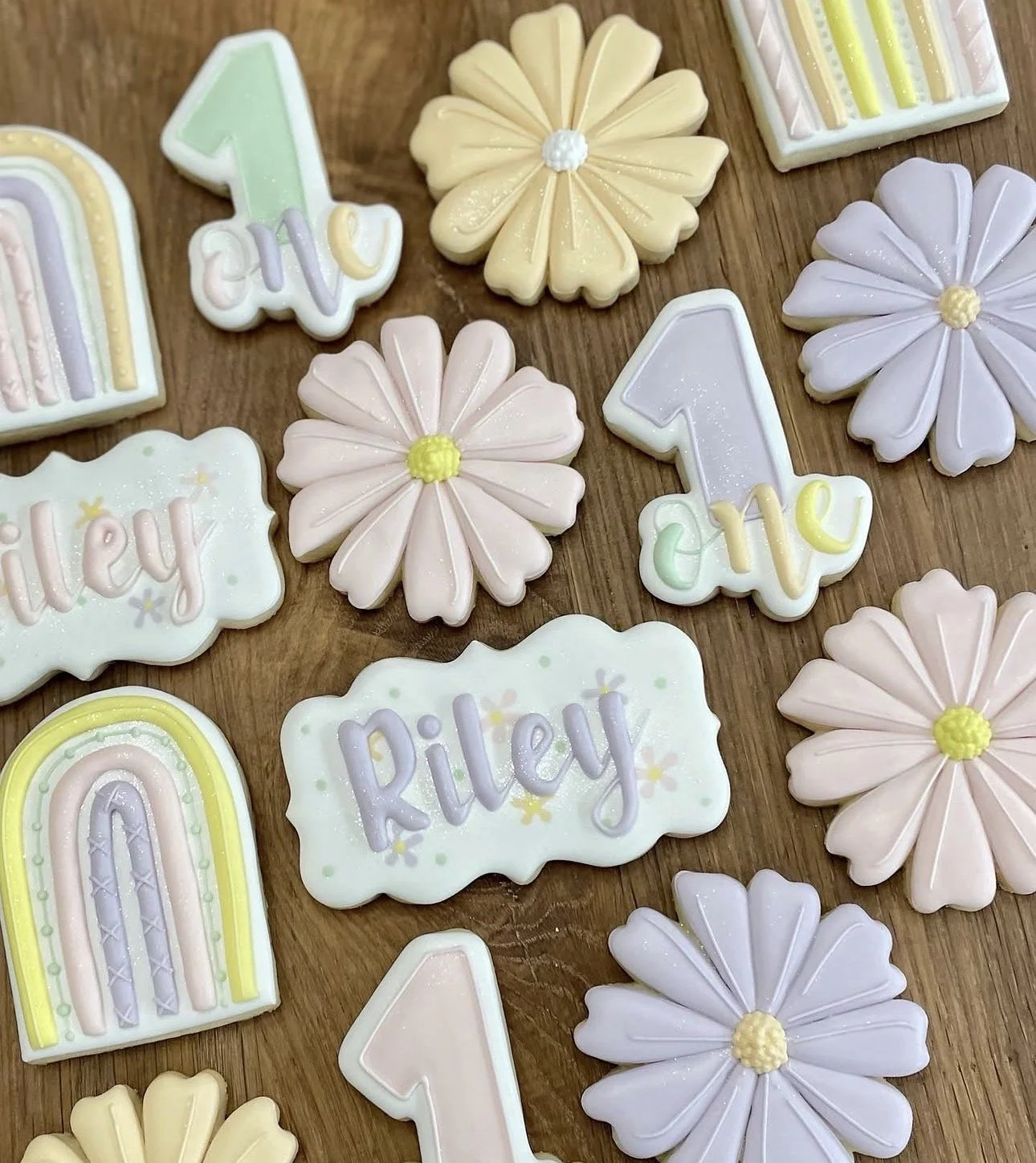 Pastel flower and rainbow cookies with raised number-one designs and names Riley and Ellie on a wooden table