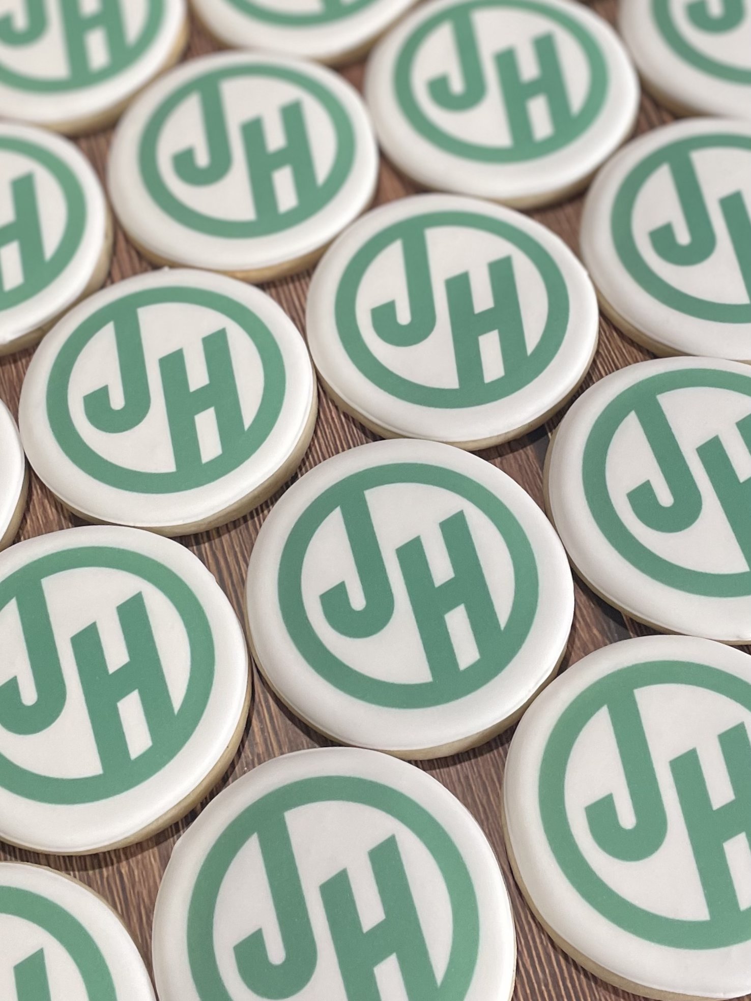 White round cookies with green monogram logos arranged on a wooden surface