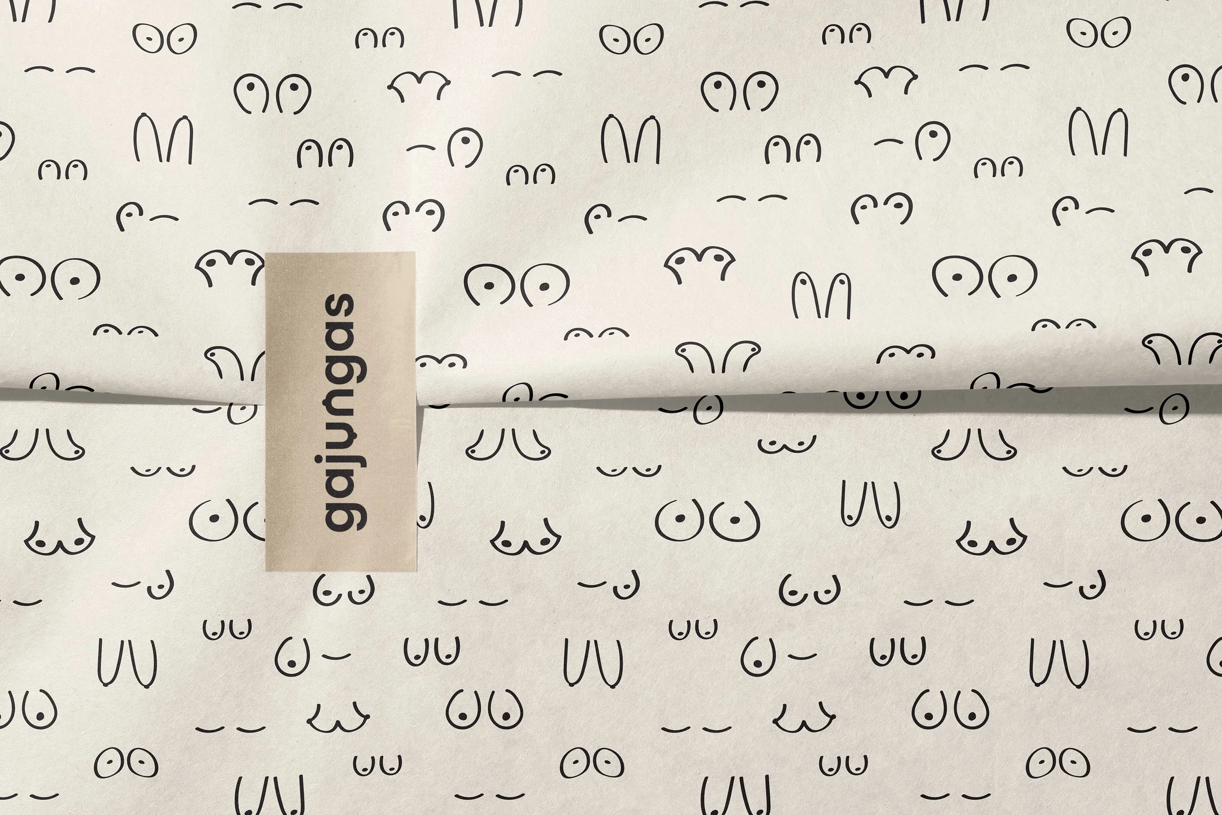 Close-up of a sheet of paper with a pattern of black line drawings of bunny faces, pair of eyes, and noses. There is a beige label with the word 'greetings' printed on it partially covering the paper.