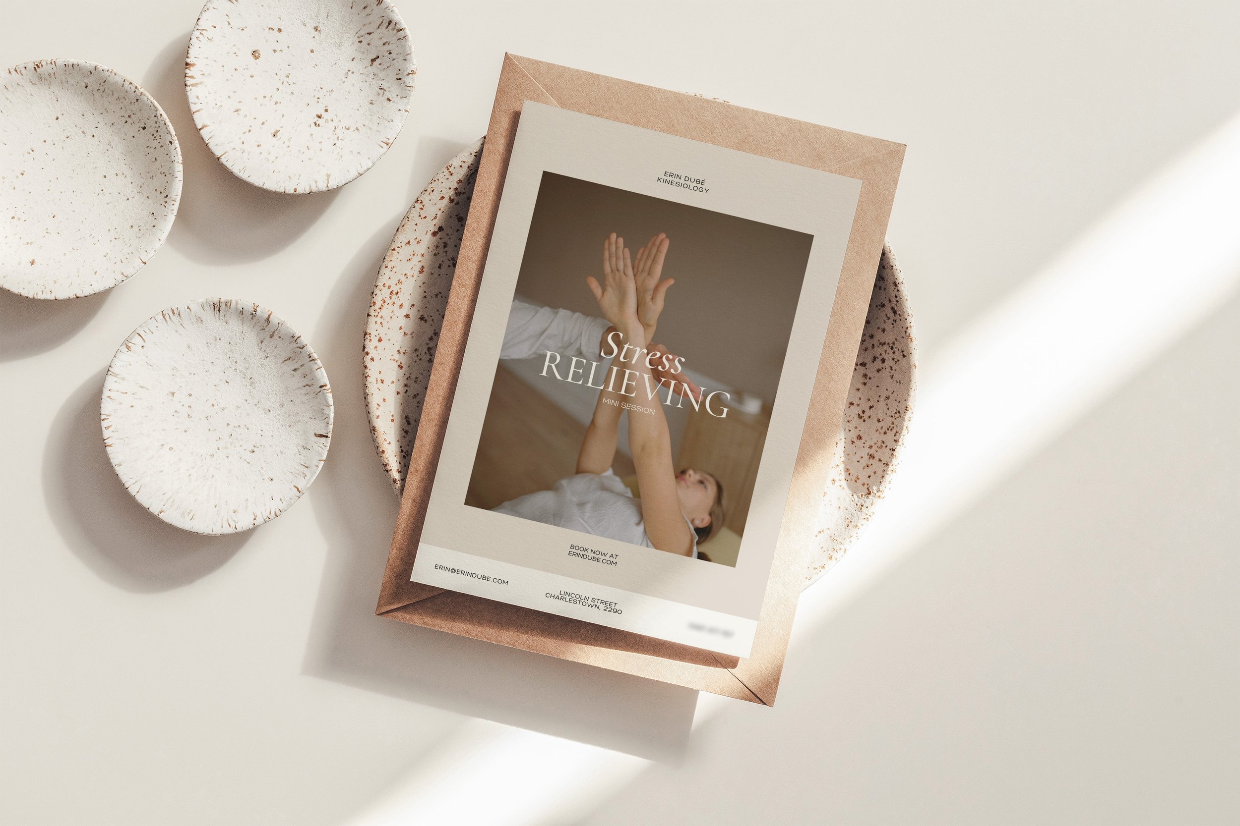 A flyer advertising stress relieving mini sessions featuring a photo of a person lying down with hands raised. The flyer is placed on a brown envelope, surrounded by four white speckled ceramic plates on a white surface.