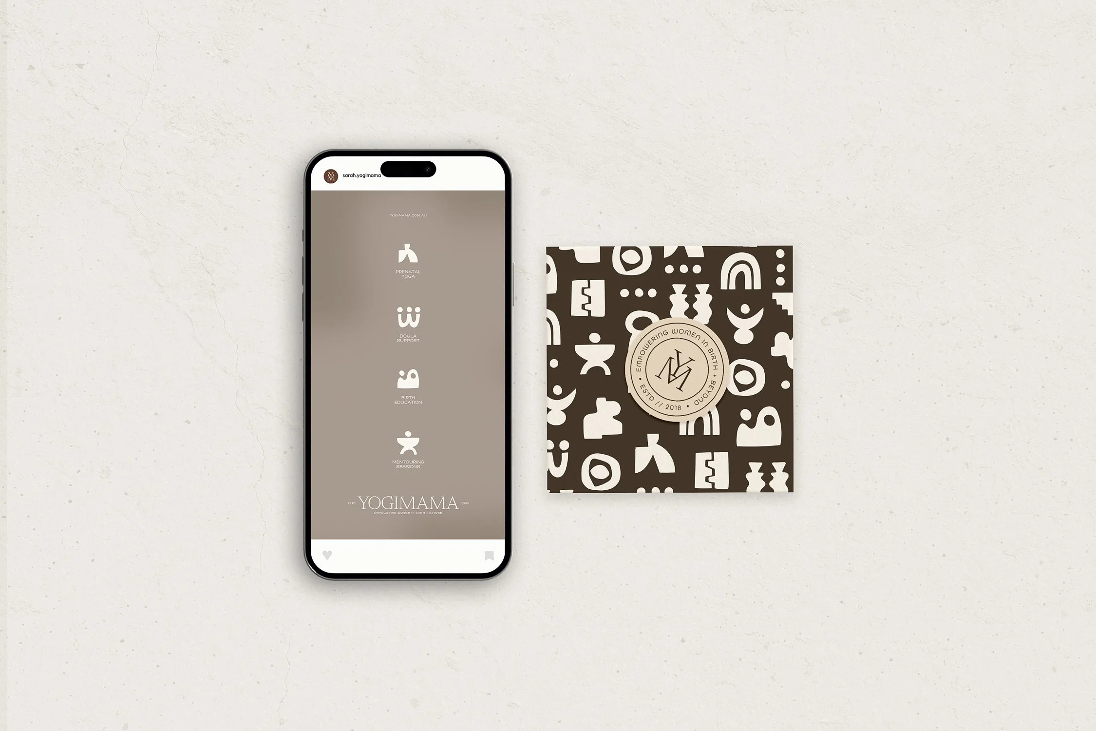 Smartphone displaying a website with categories related to prenatal yoga, doula support, birth education, and mentoring sessions, placed on a white surface next to a black and white patterned card with a logo and text about empowering women in birth.