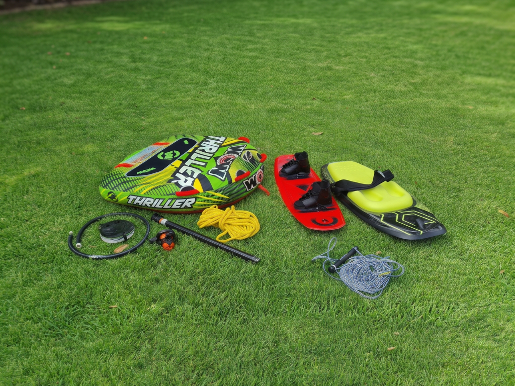 Water sports equipment including a wakeboard, wakeboard boots, a life vest, a tow rope, a helmet, a leash, and a slackline laid out on a grassy lawn.