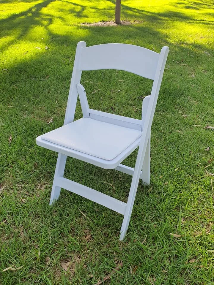 White folding chair on green grass with a tree in the background.