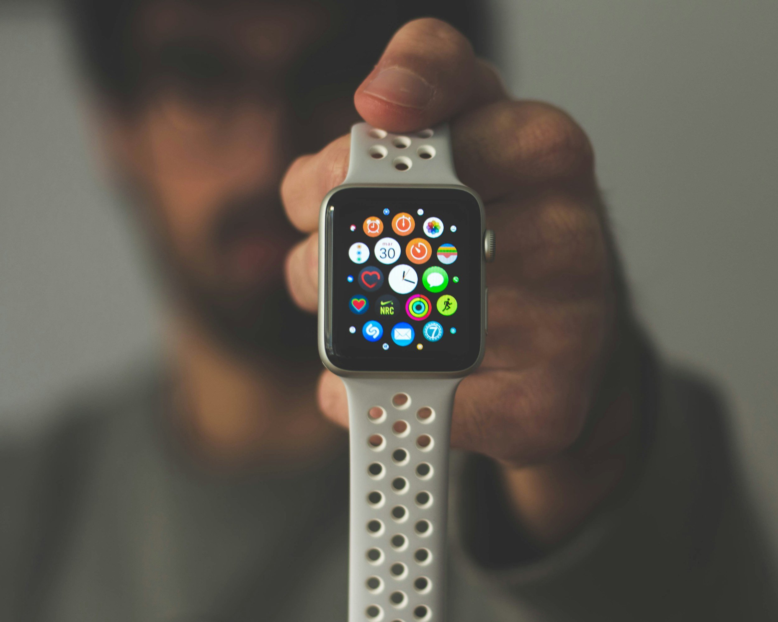 Close-up of a person's hand holding a smartwatch with a colorful app display, and a white perforated wristband.