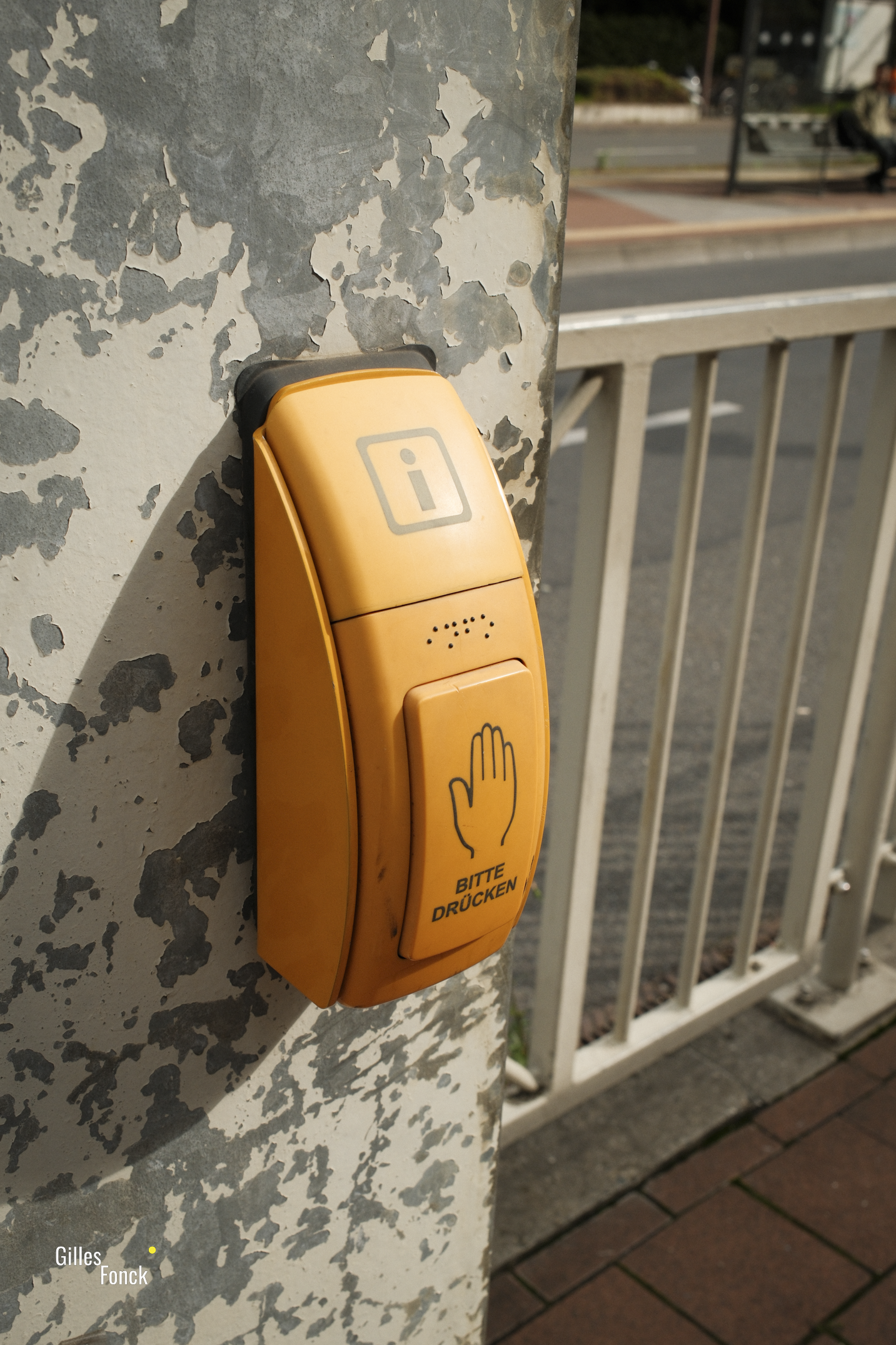 A bright yellow assist button for visually impaired people at a publich transit stop.