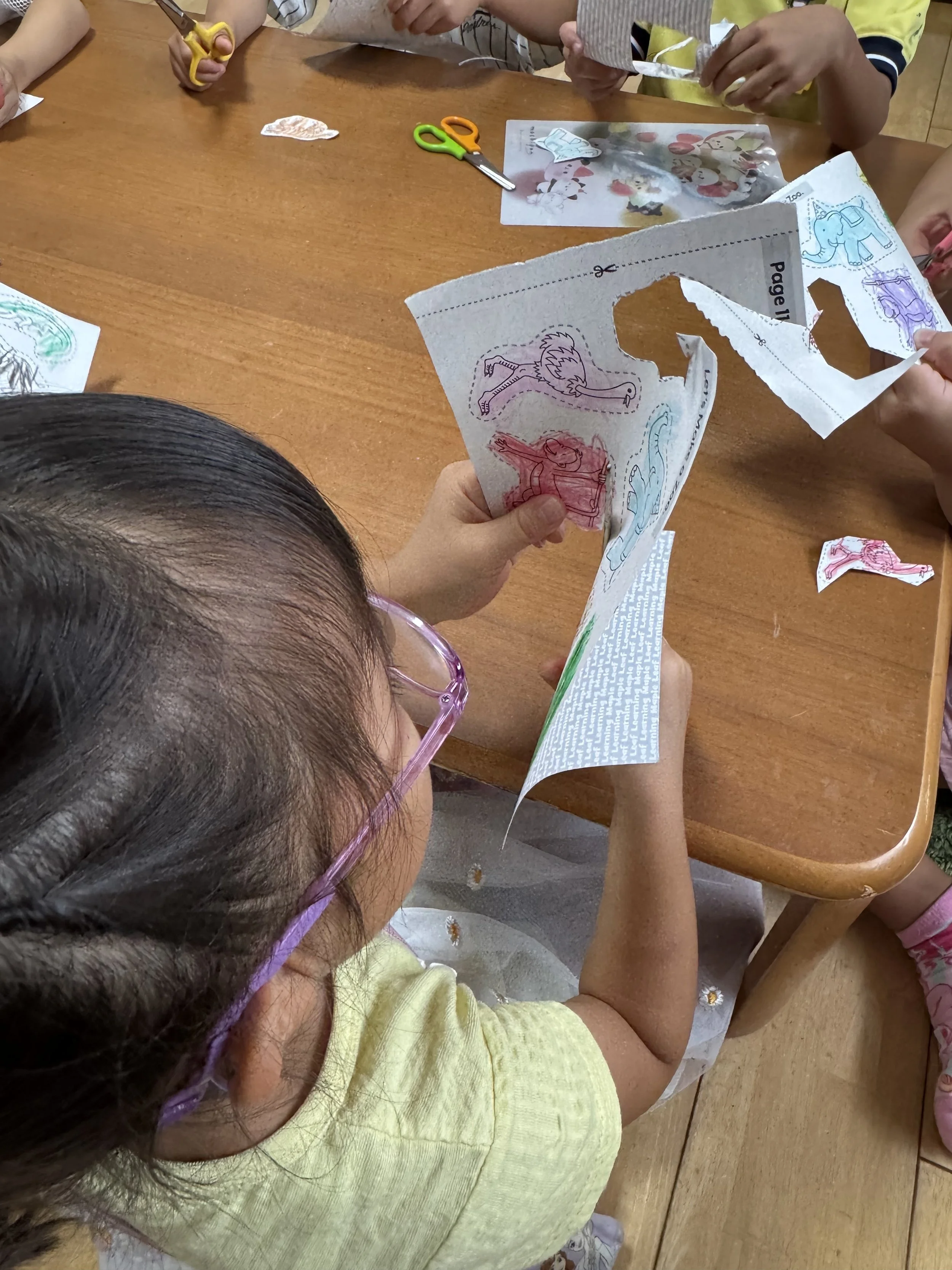 子どもたちが木製テーブルで色紙の動物イラストをはさみで切り抜く工作をしている様子