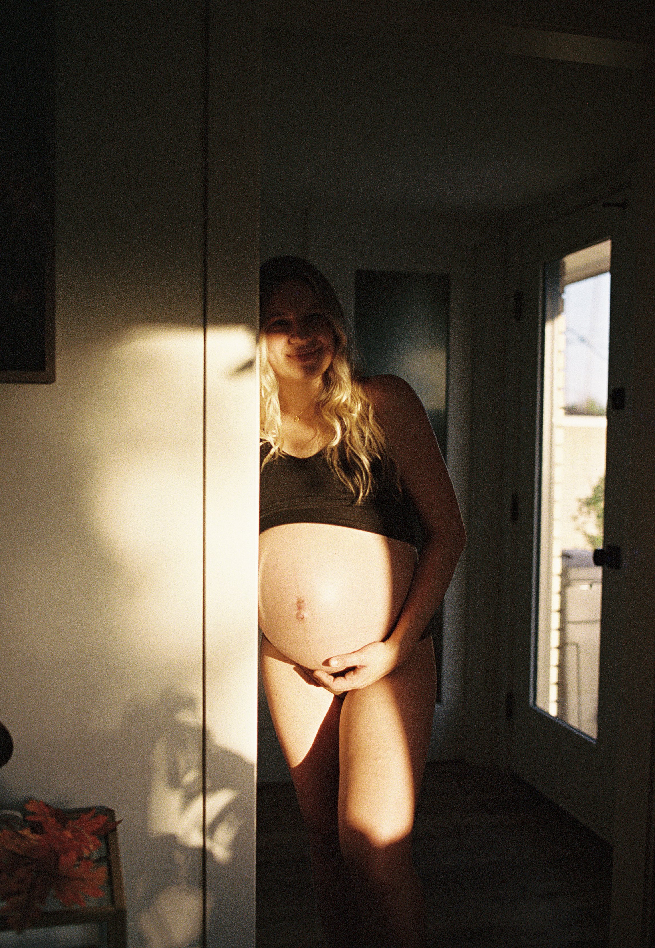A pregnant woman leaning in a doorframe, posing for a maternity photo. Light is illuminating her belly.