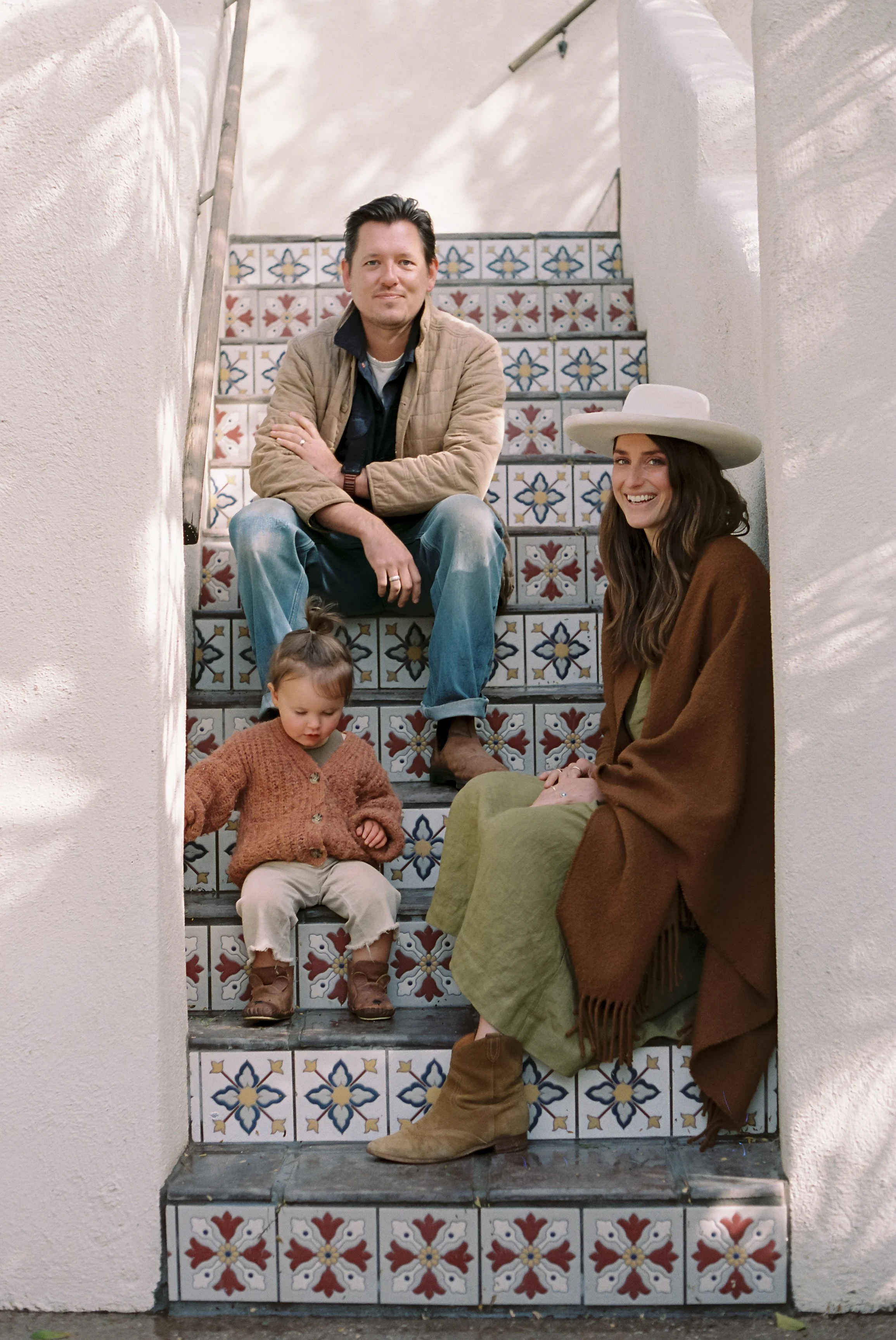 A family of four posed for a portrait on decorative tiled steps inside a building. The staircase has white walls and colorful patterned tiles.