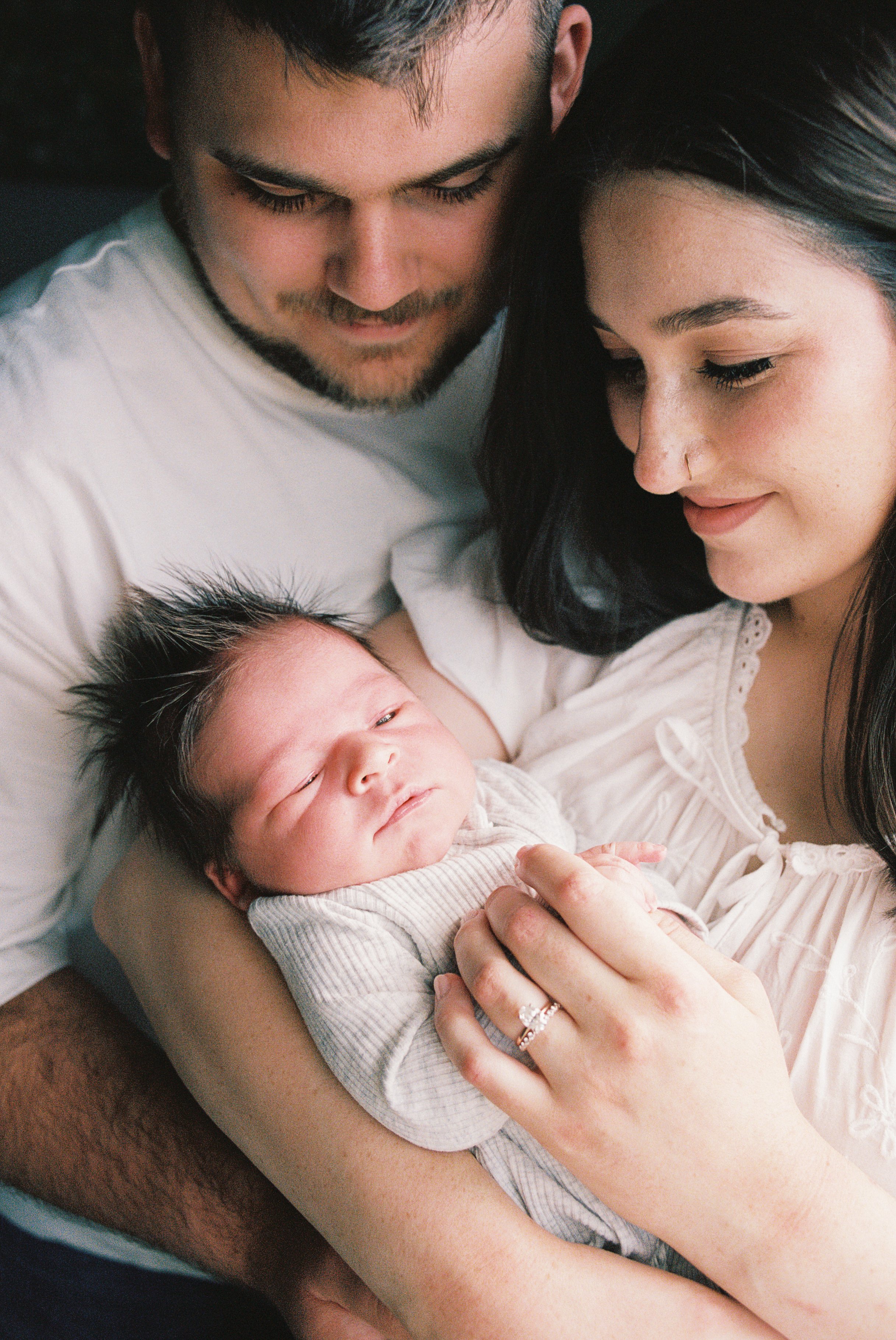 A family scene showing a woman and a man holding a newborn baby, all looking at the baby lovingly.