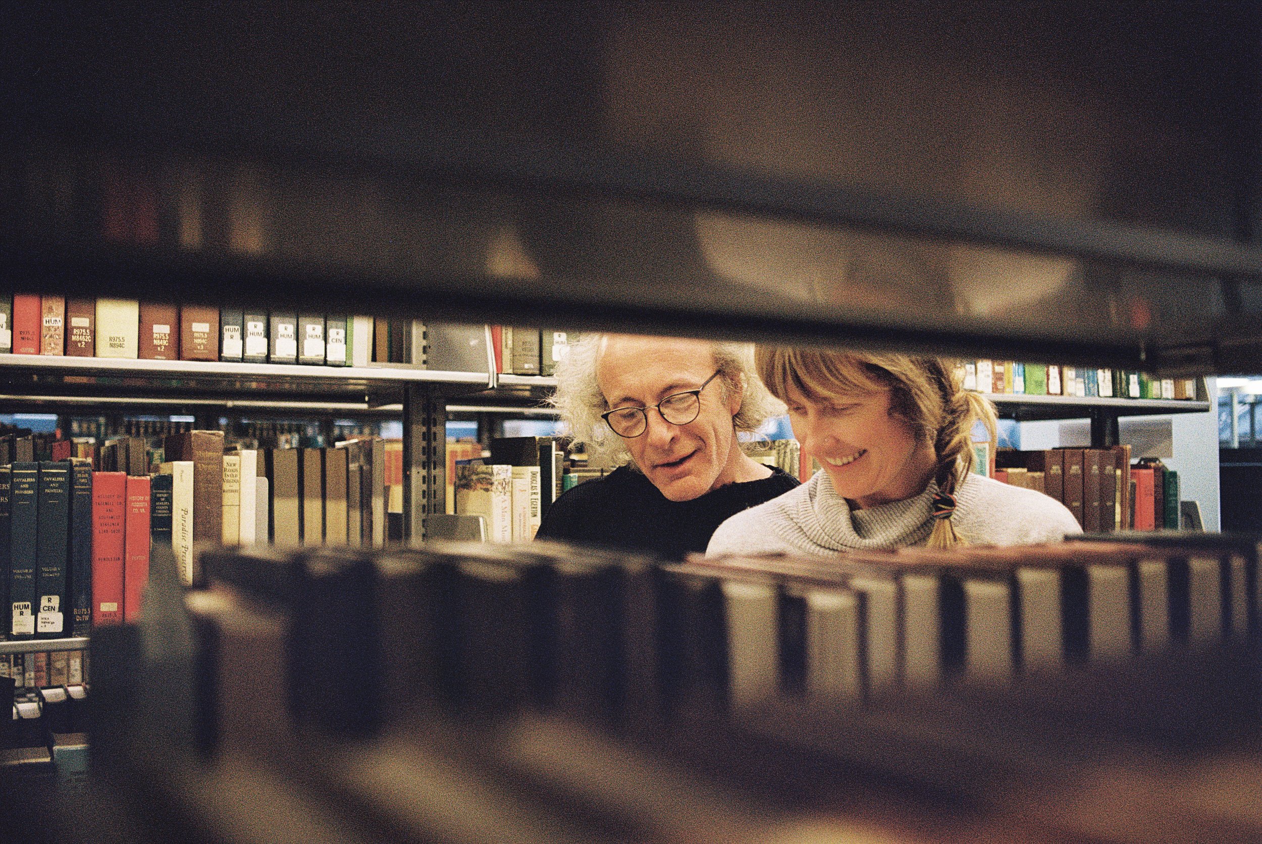 A couple looking at books on a shelf in a library.