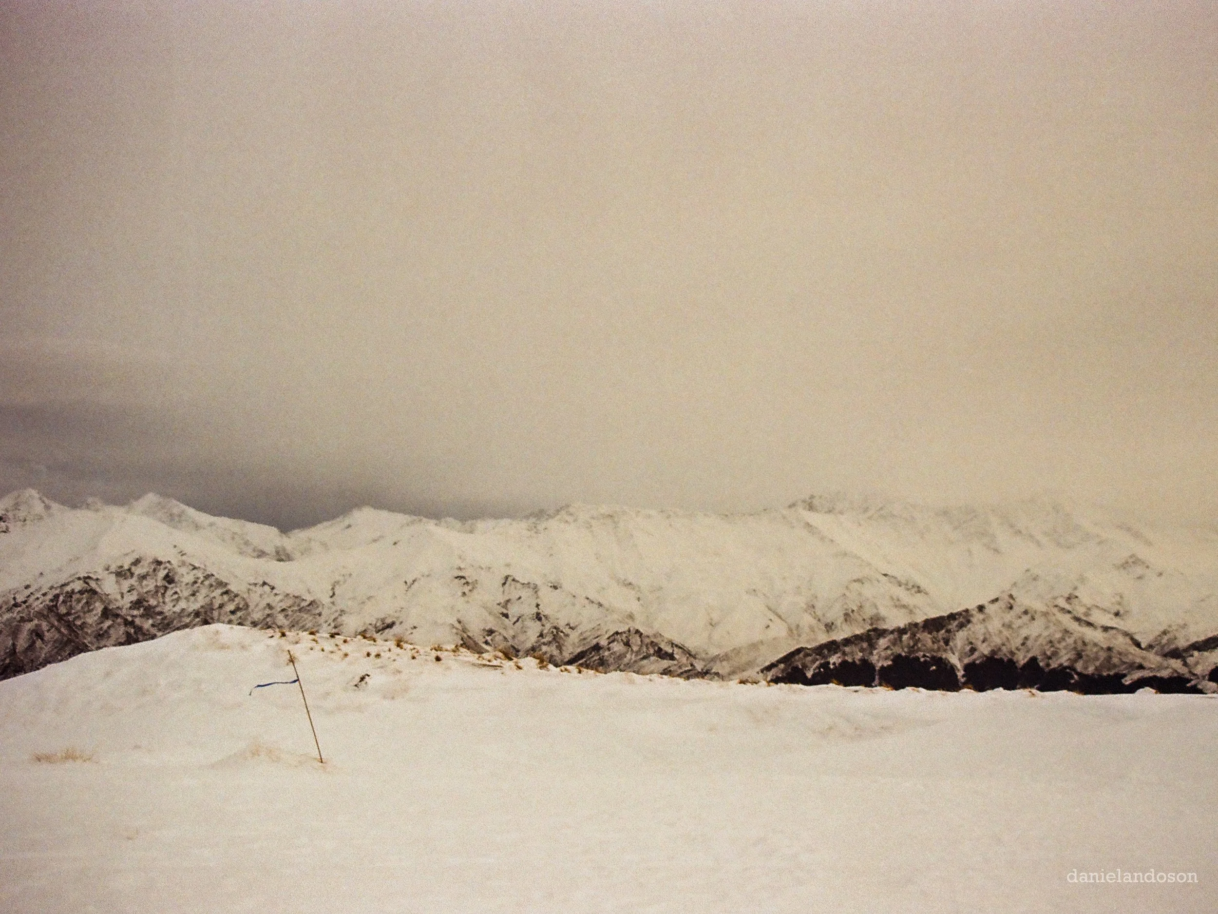 Snow-covered mountain peaks under a cloudy sky with some snow in the foreground.