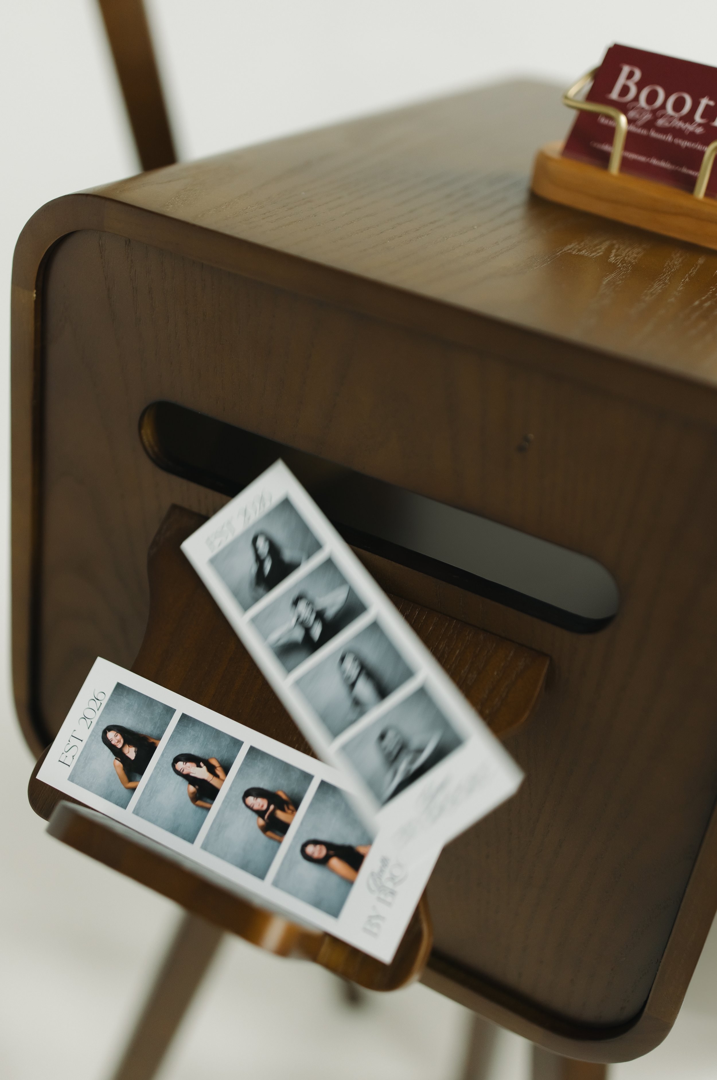 Wooden table with a photo strip of a woman with long dark hair, seated and posing in front of a gray background.