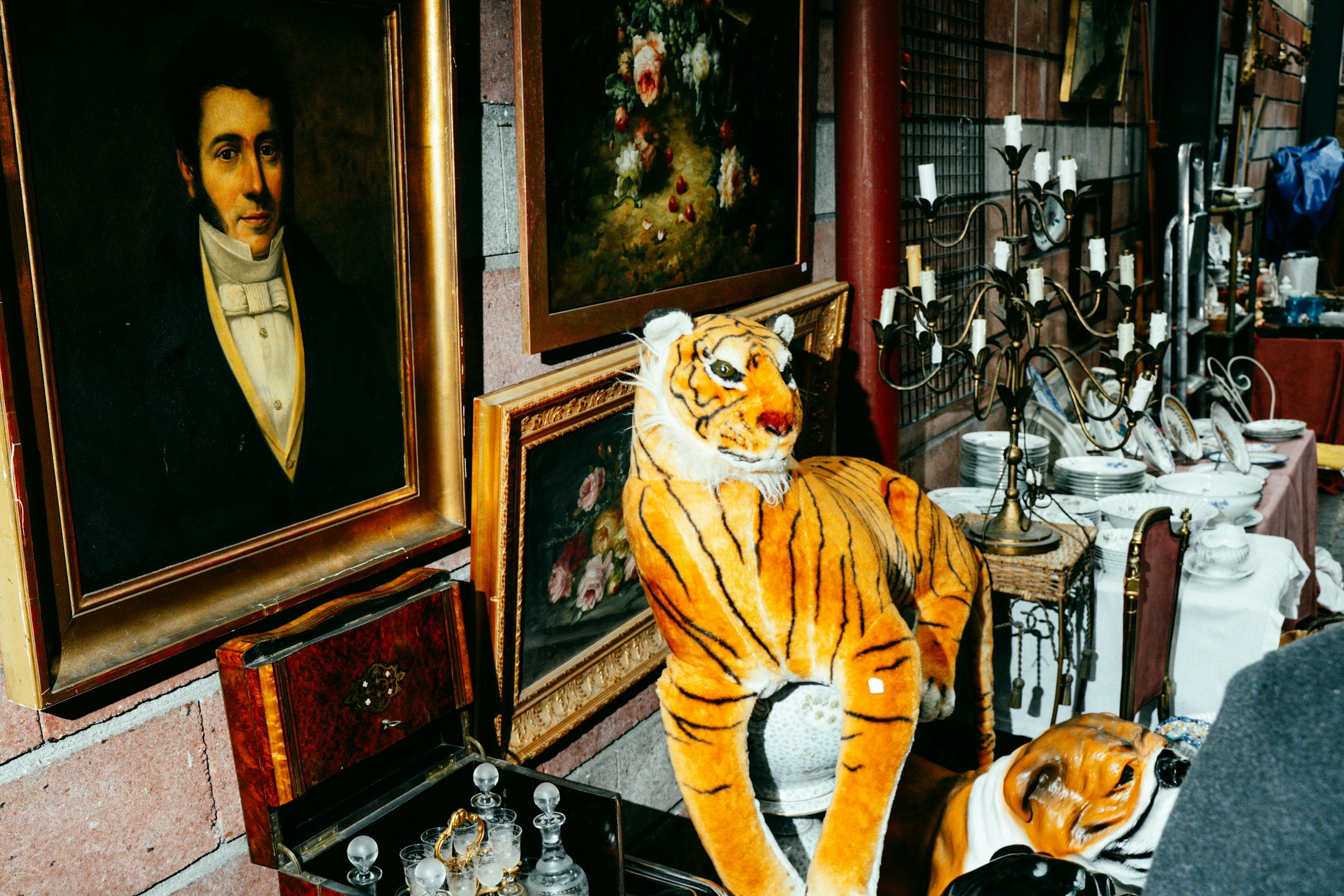 A collection of vintage paintings, a tiger stuffed animal, and various antiques displayed at an outdoor sale or flea market.