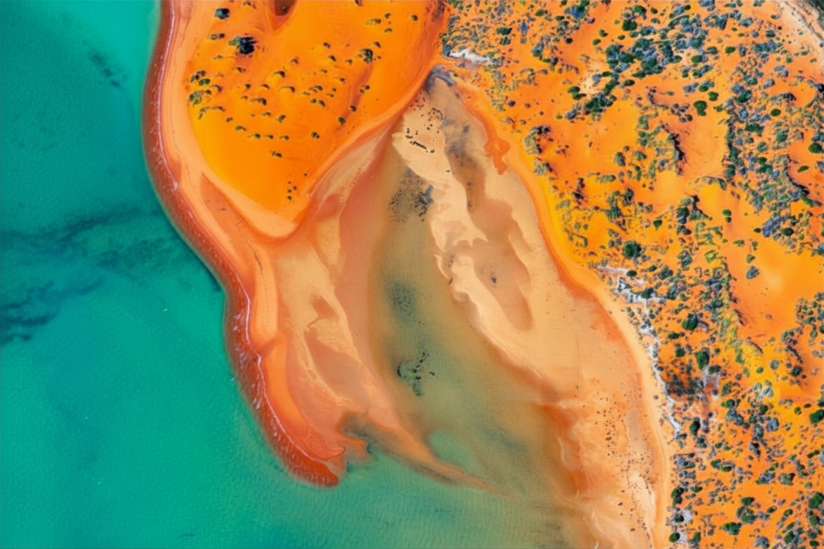 Aerial view of a colorful coastal landscape with turquoise water, orange land, and green vegetation.