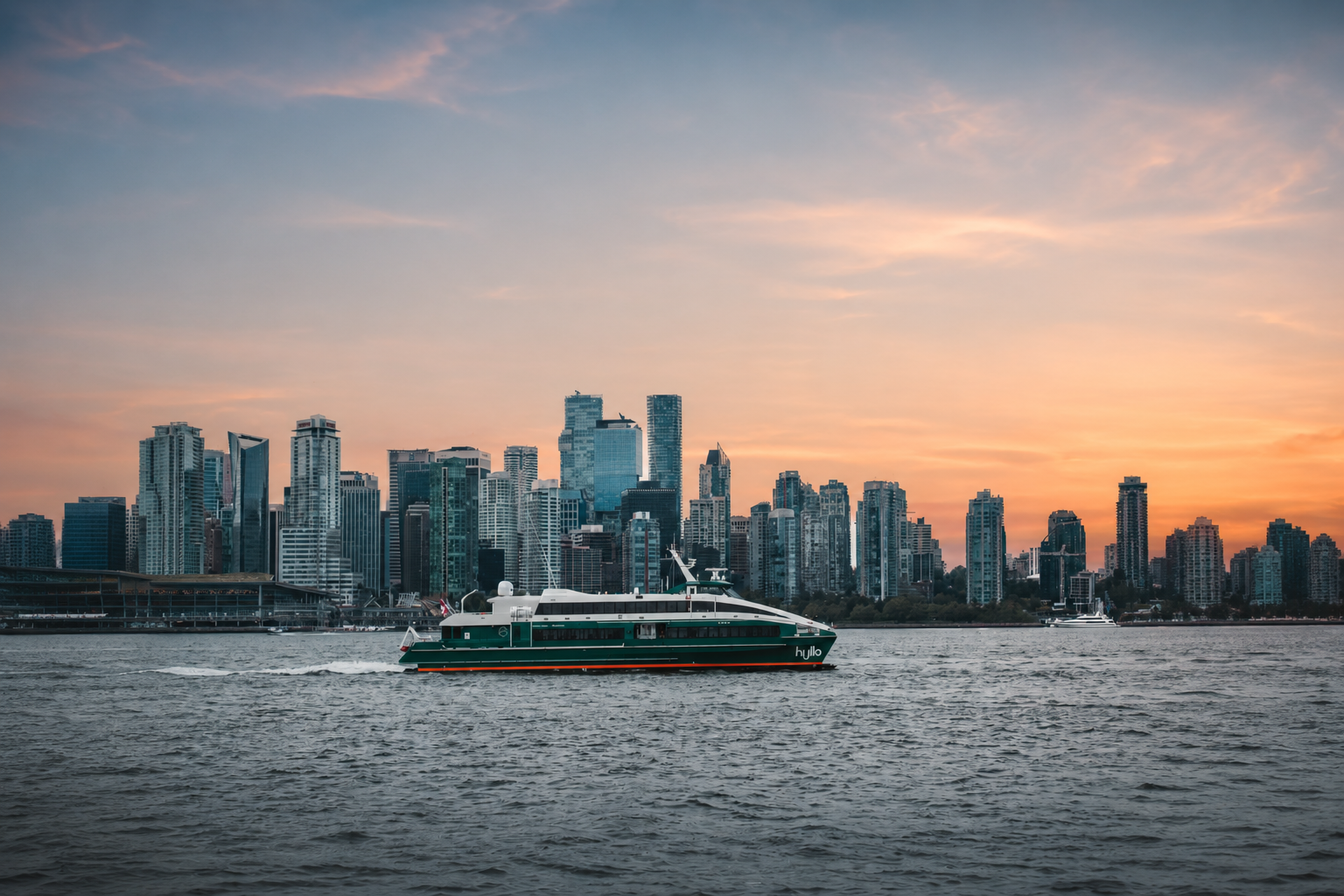 A yacht sailing on a river in front of a city skyline at sunset.