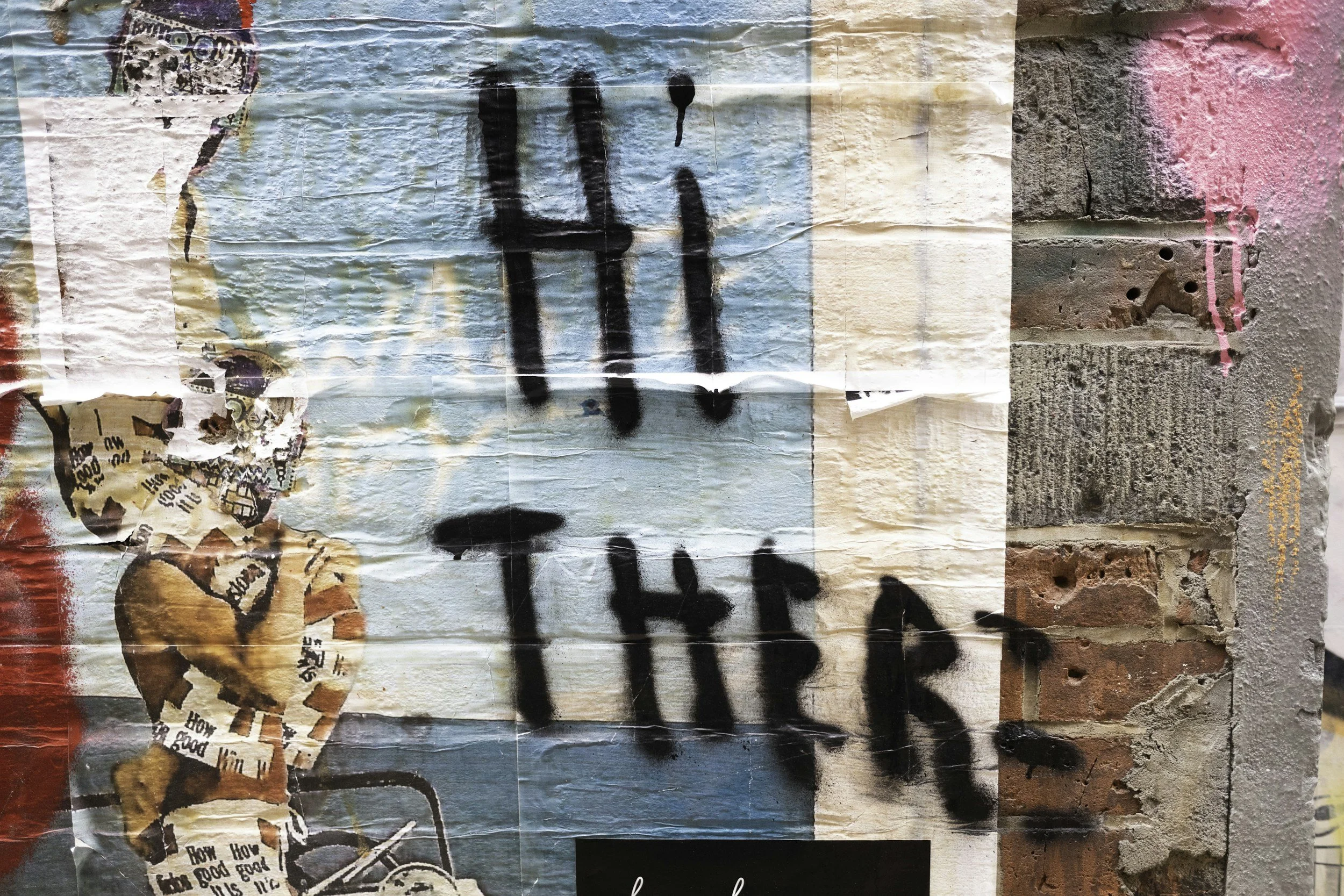 Graffiti on a brick and concrete wall with black spray-painted words and colorful posters, including an image of a dog and torn pieces of advertisements or flyers.