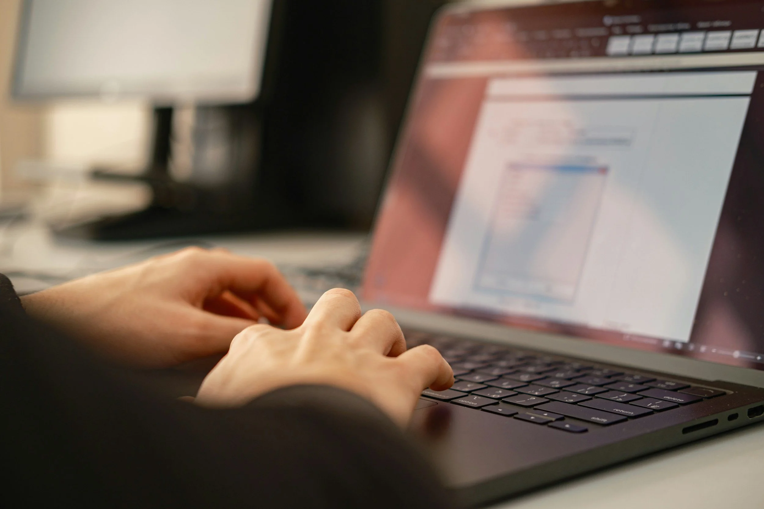 Person typing on a laptop computer with a colorful screen, in a dimly lit environment.